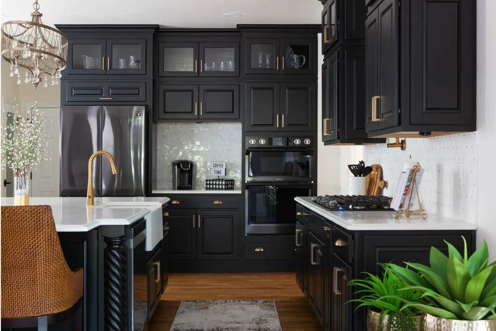 A modern kitchen features black cabinetry, white countertops, a large island with a gold faucet, and a subway tile backsplash.