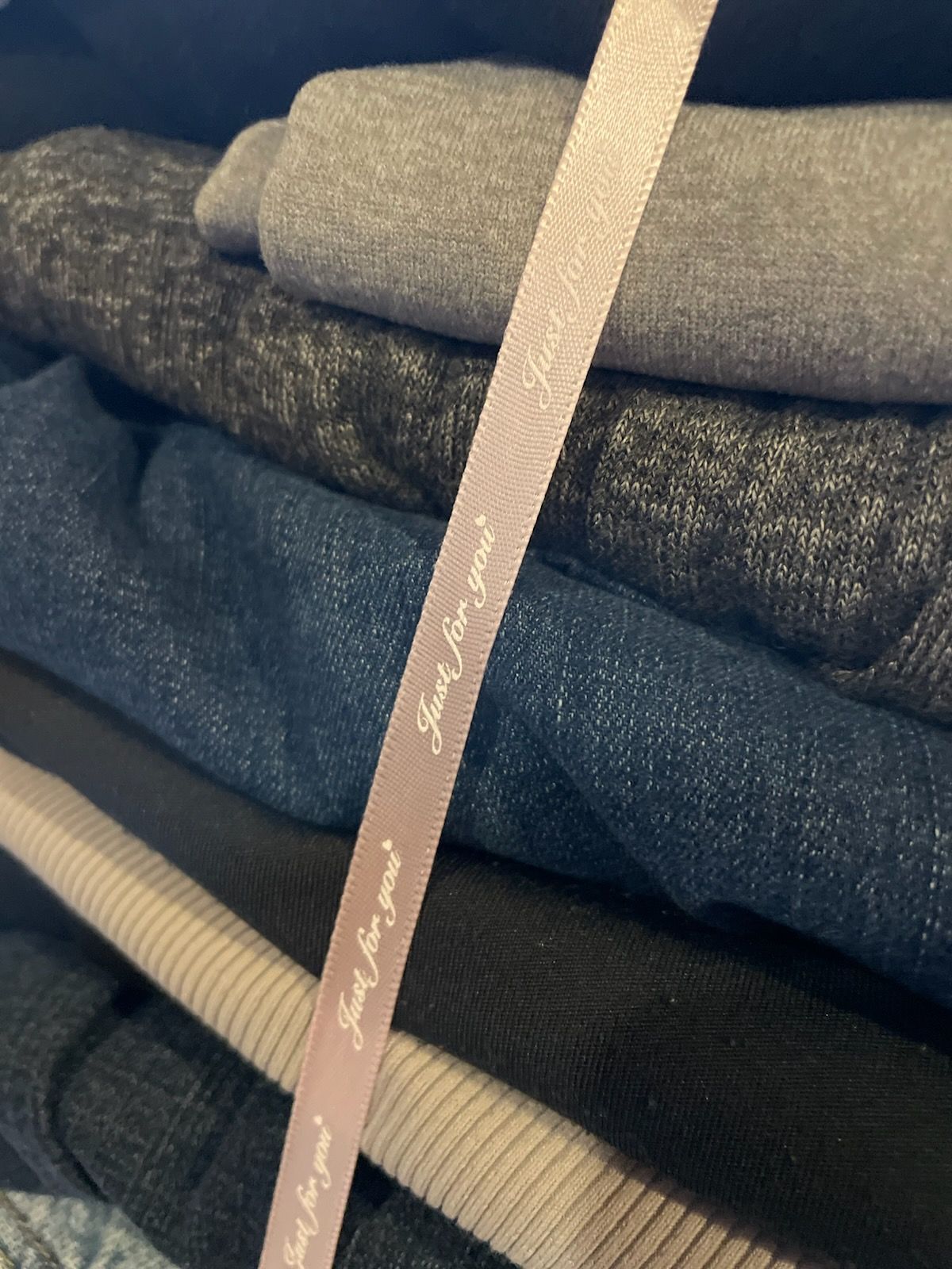 Stack of folded clothes with a light pink ribbon that reads 