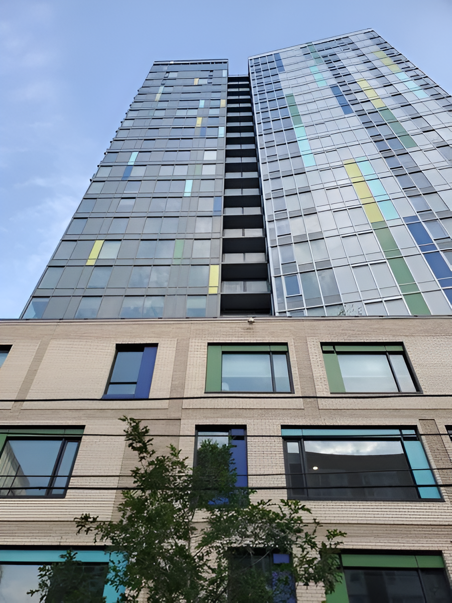 Tall modern skyscraper with colorful glass panels and lower building with windows, against a blue sky.