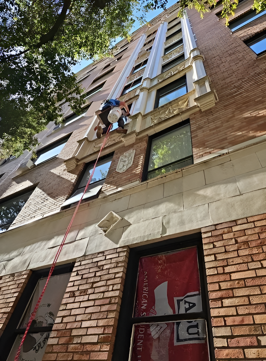 A person rappelling down a tall brick building, fixing the facade.