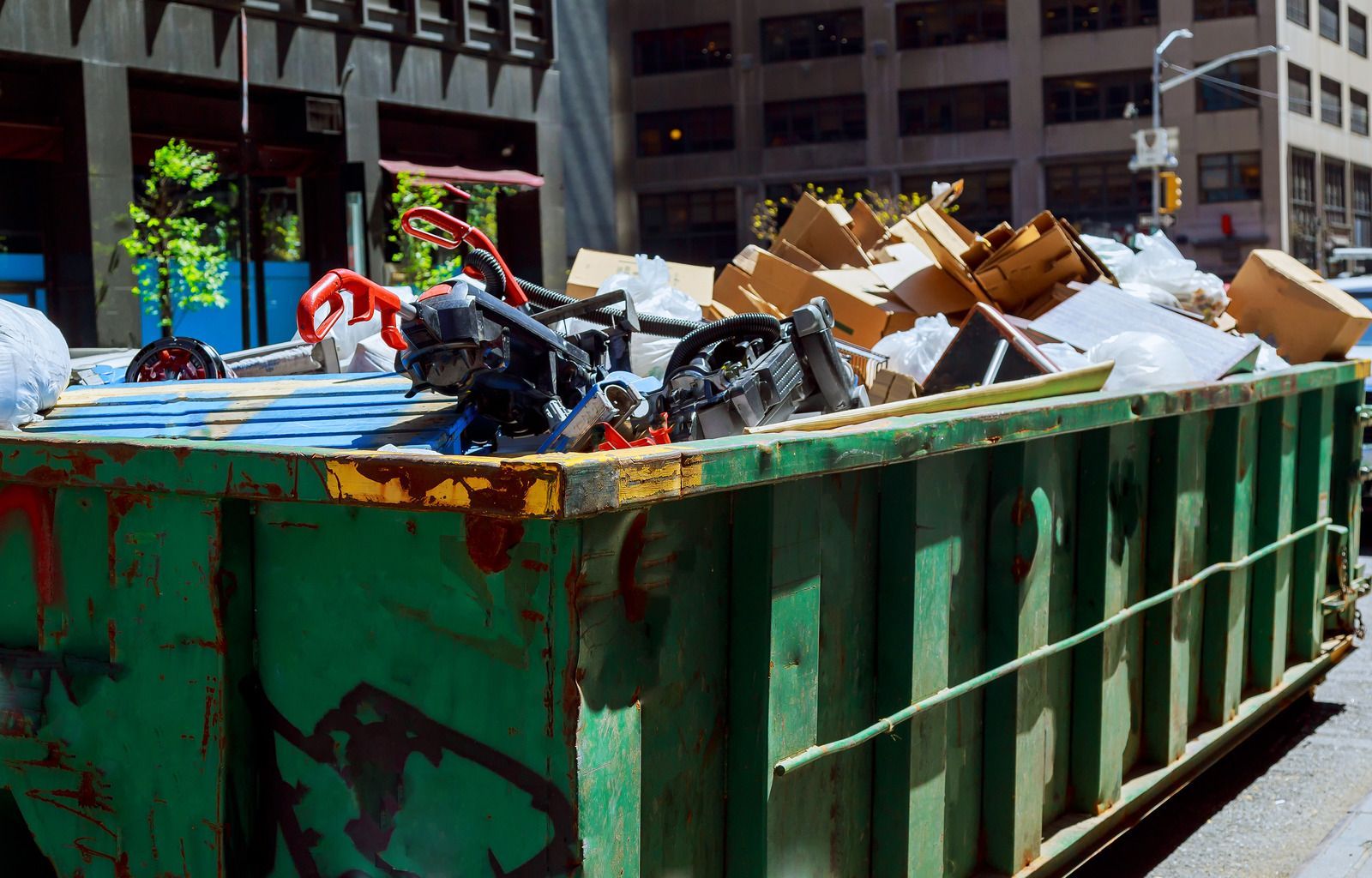 A green dumpster filled with garbage is parked on the side of the road.