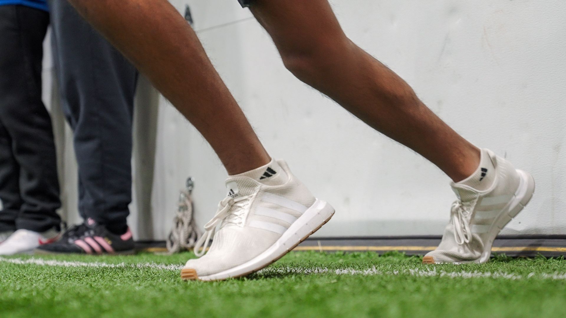 Runner in white Adidas sneakers on a green track. Legs bent in motion.
