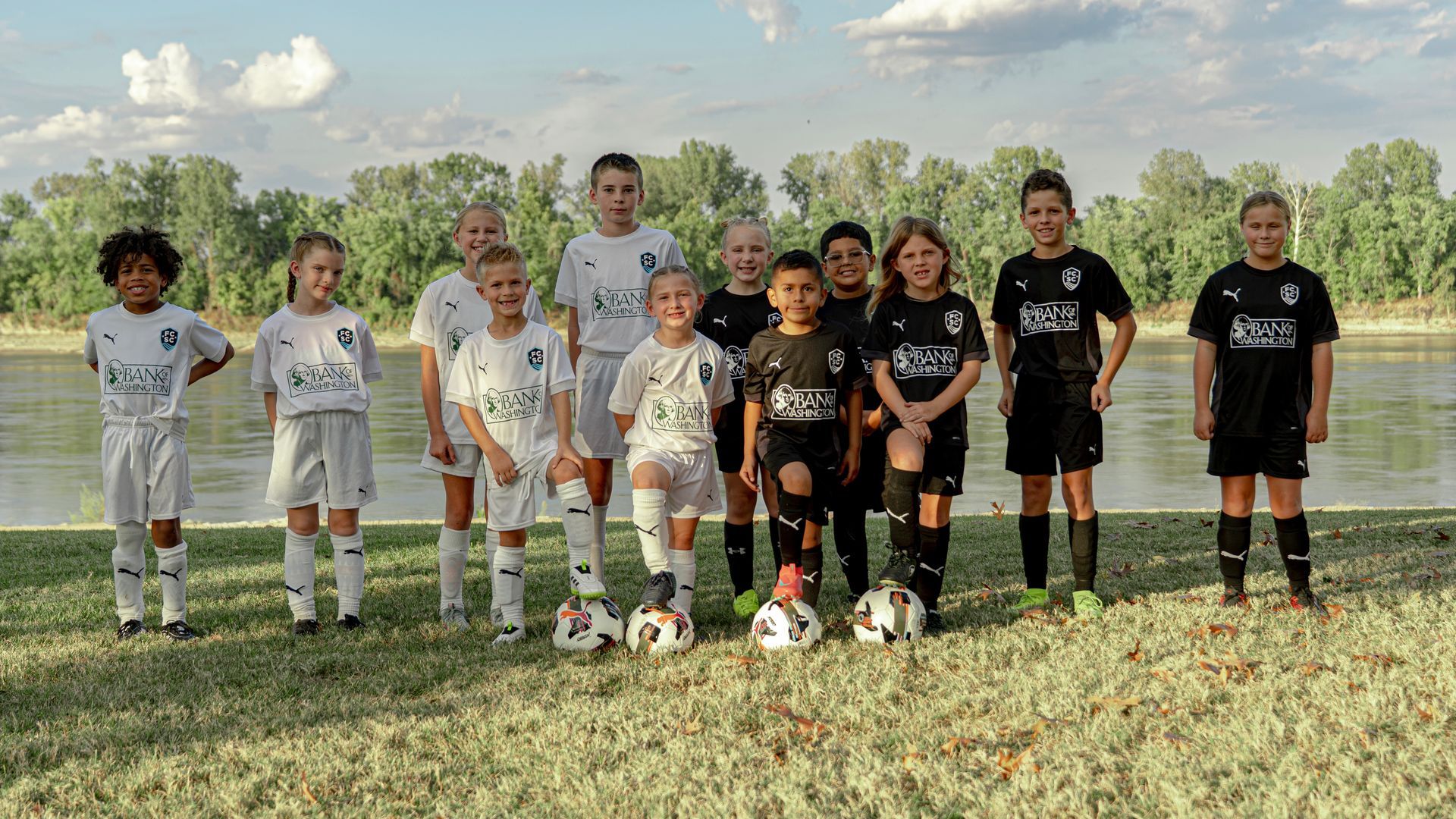 Children in soccer gear gather around a coach on an indoor turf field.