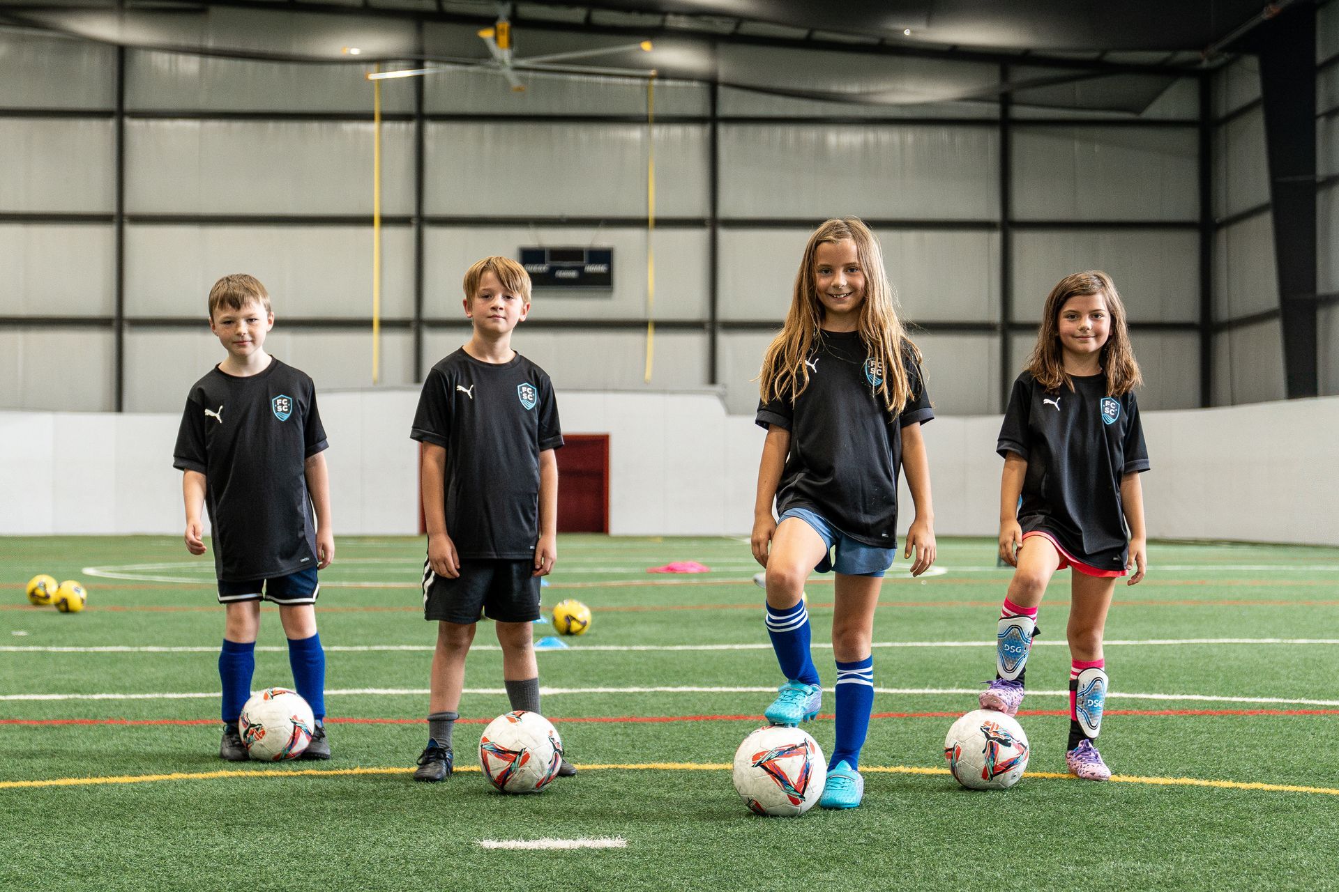 Boy in black soccer uniform dribbling a ball on a green indoor field.