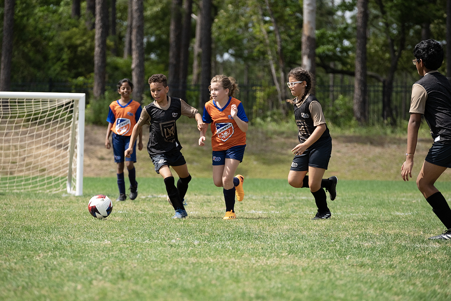 Soccer game: children running on a green field. Players in jerseys, chasing the ball near the goal.