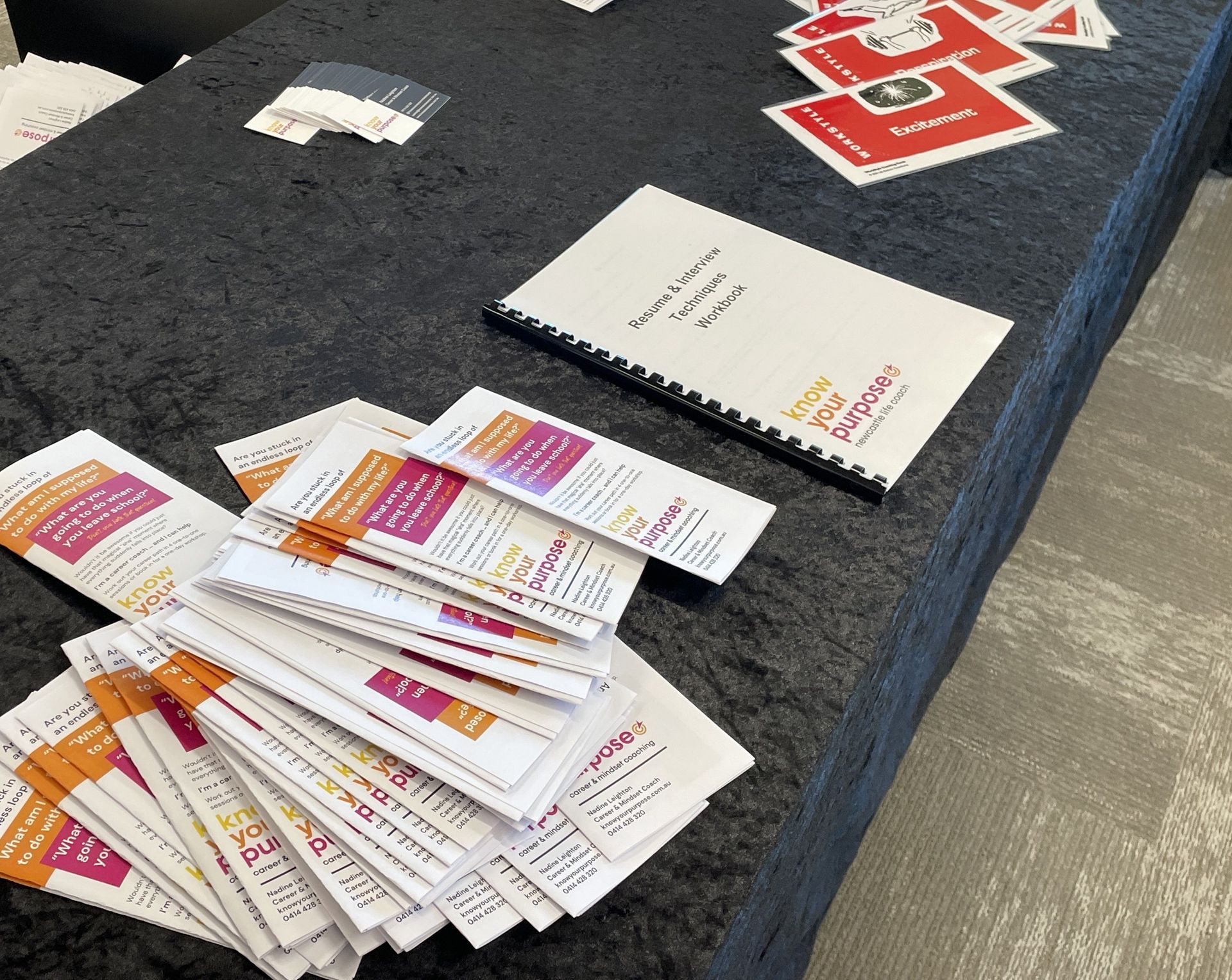 Table with event materials, including brochures, a notebook, and red-themed cards.