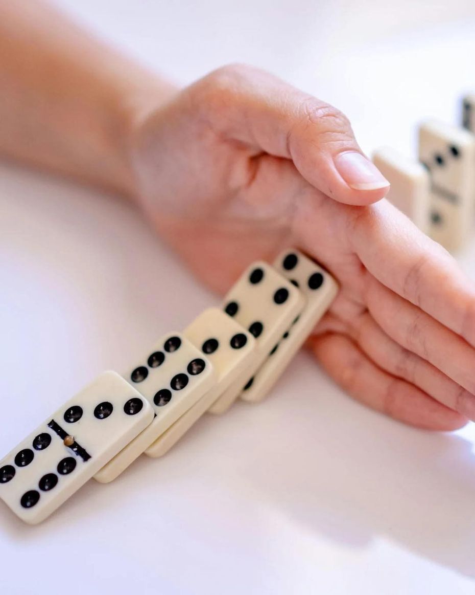 Hand stopping a row of dominoes from falling, white background.