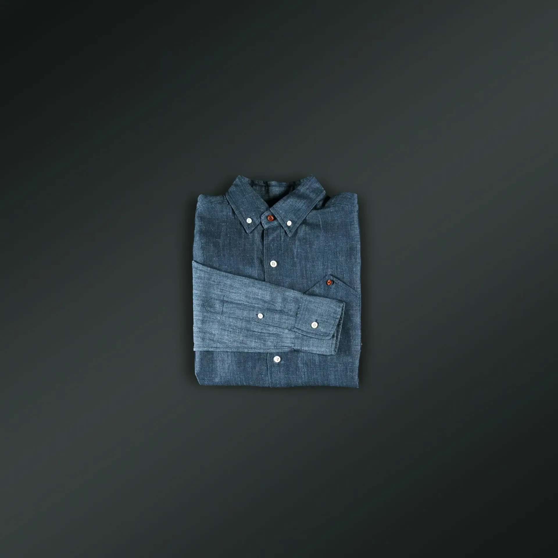 A folded denim shirt is sitting on a black surface.