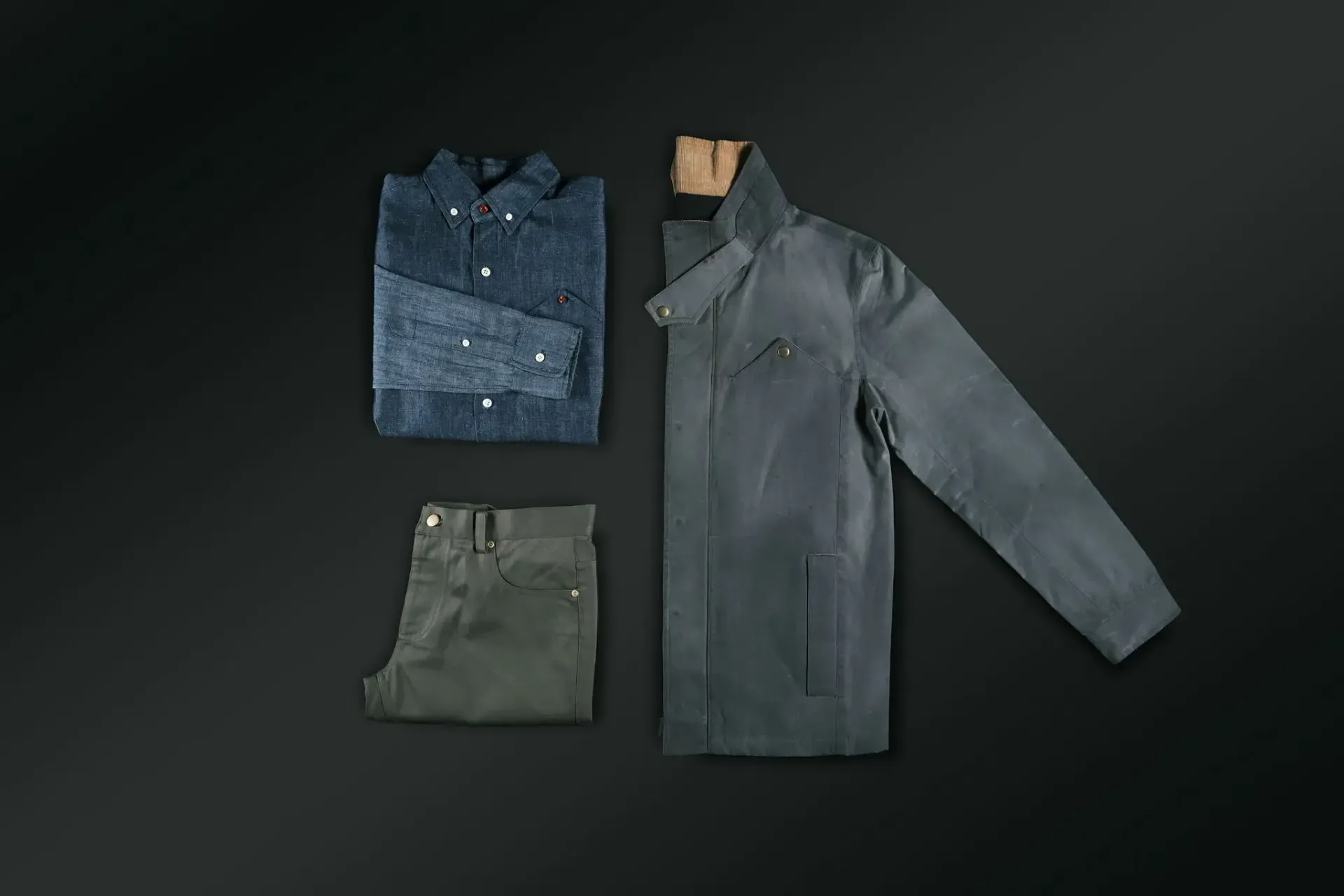 A stack of shirts , a jacket , and pants on a black surface.