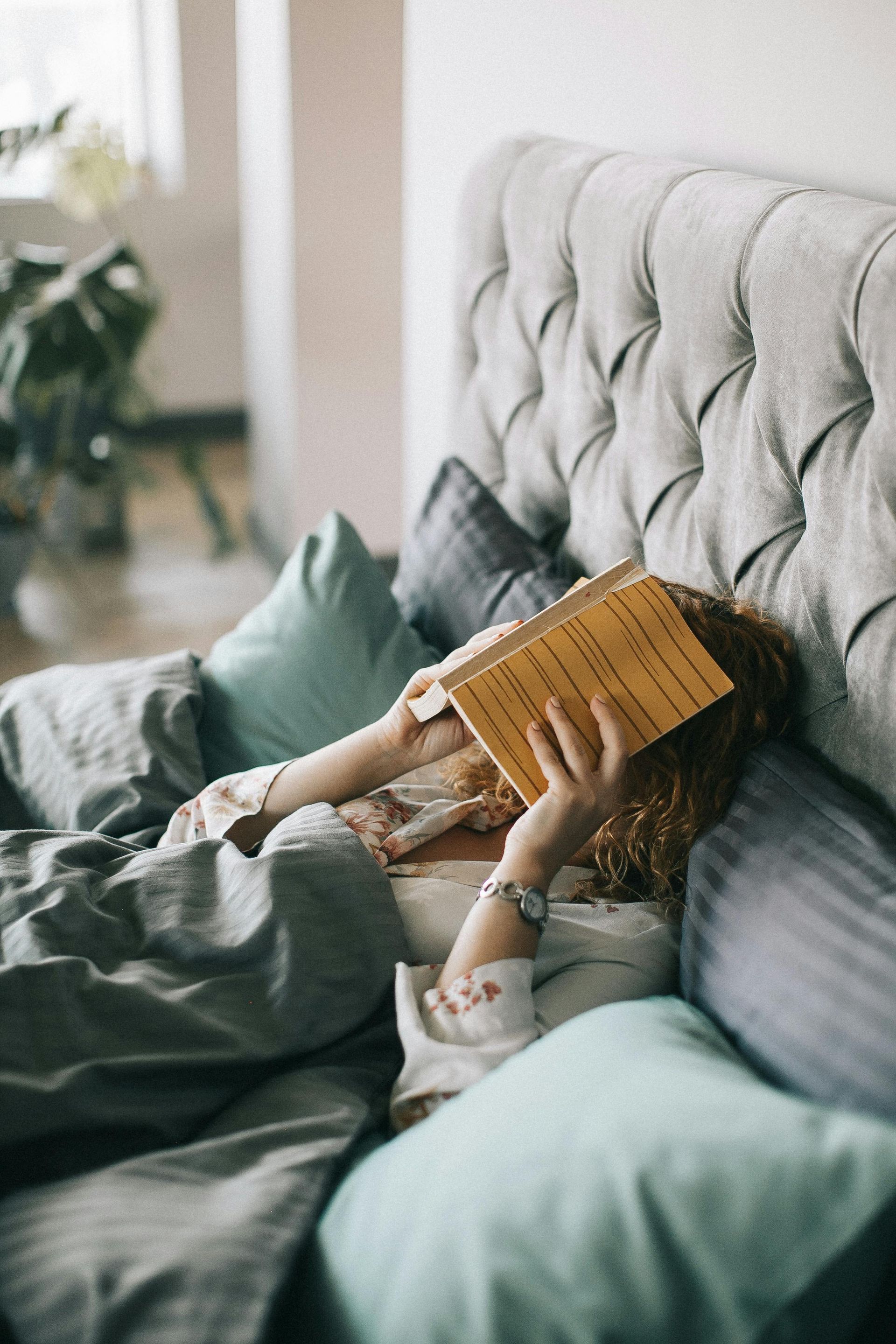 A woman is laying in bed reading a book.
