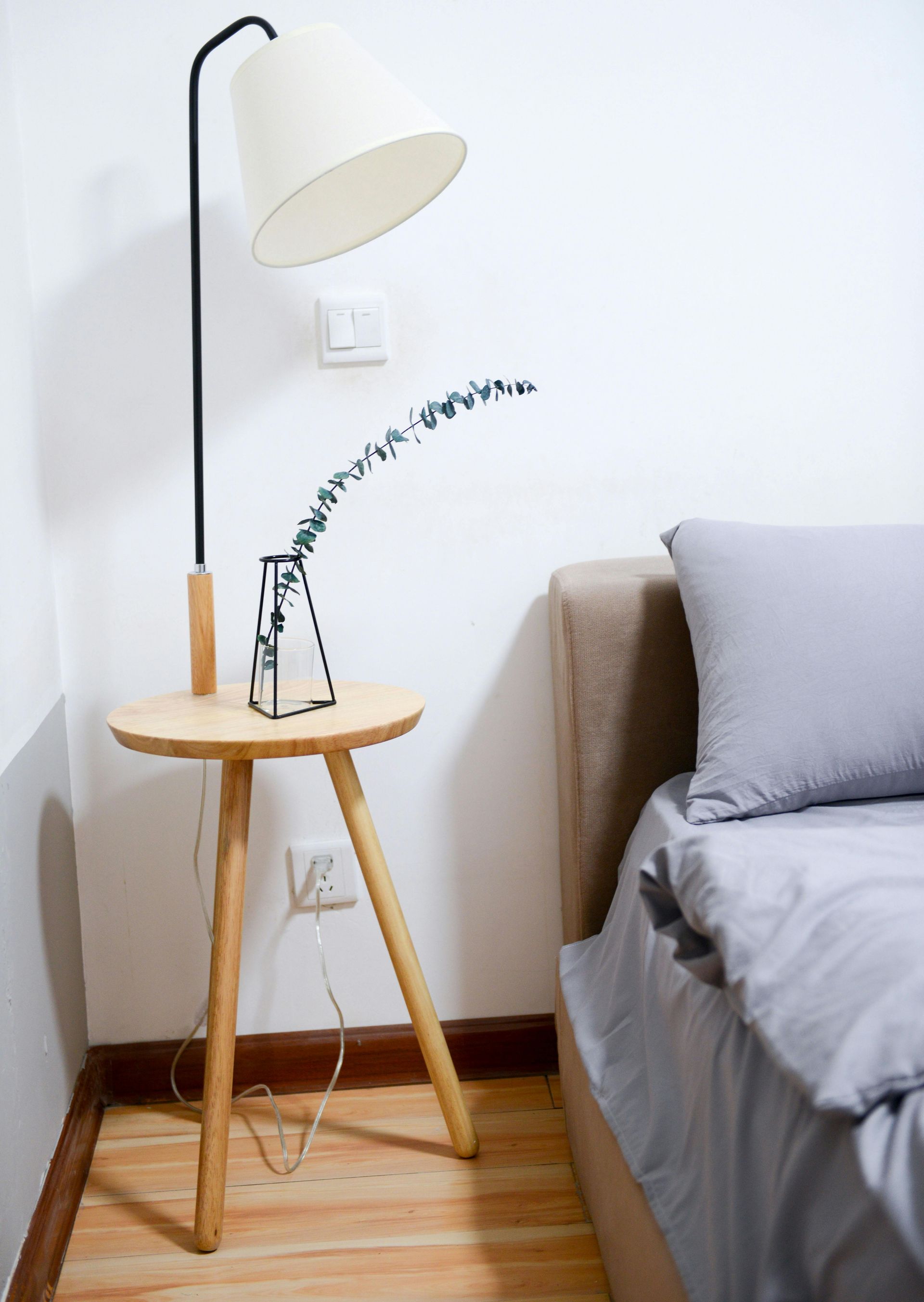 A lamp is sitting on a wooden table next to a bed.