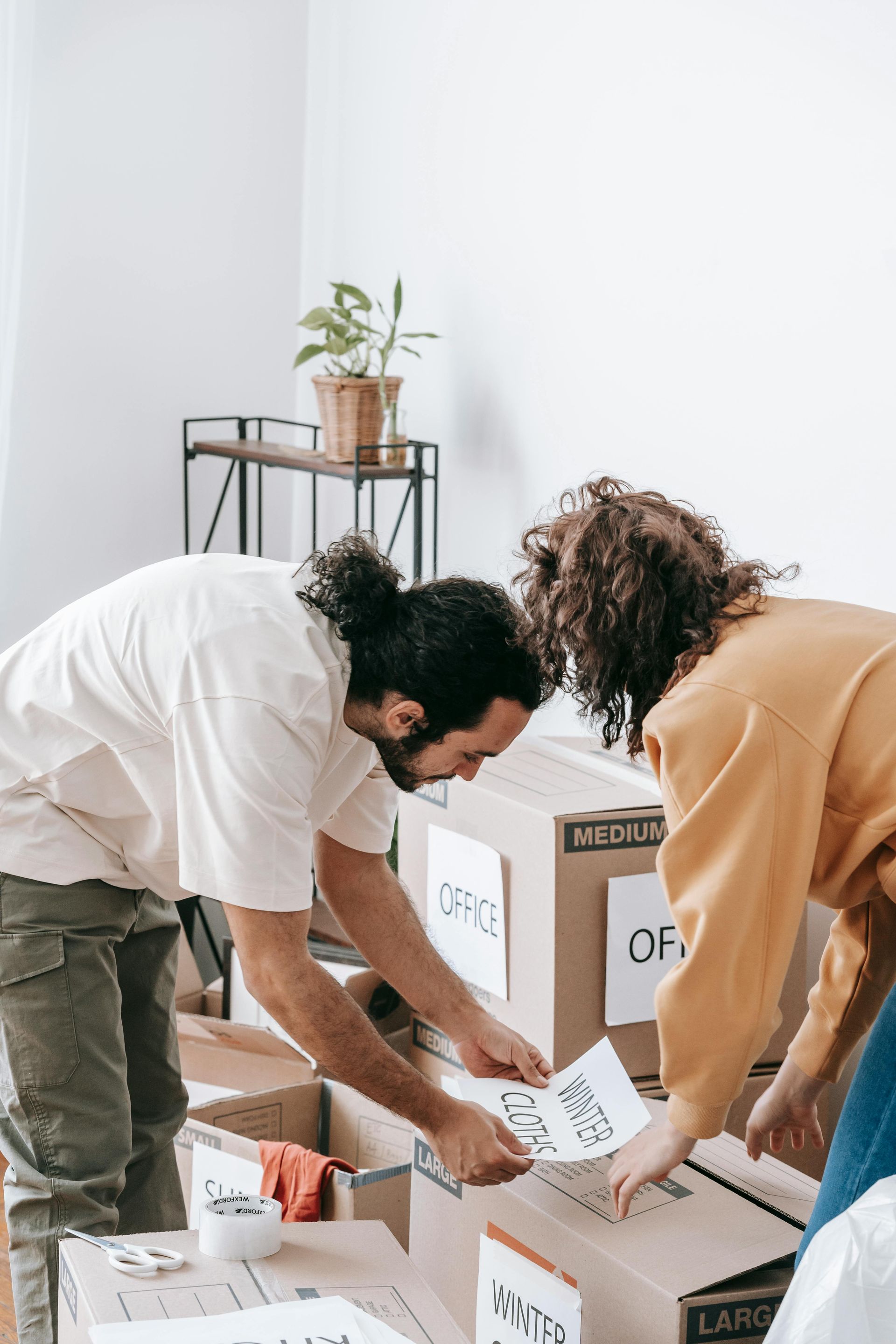 A man and a woman are packing boxes in a room.