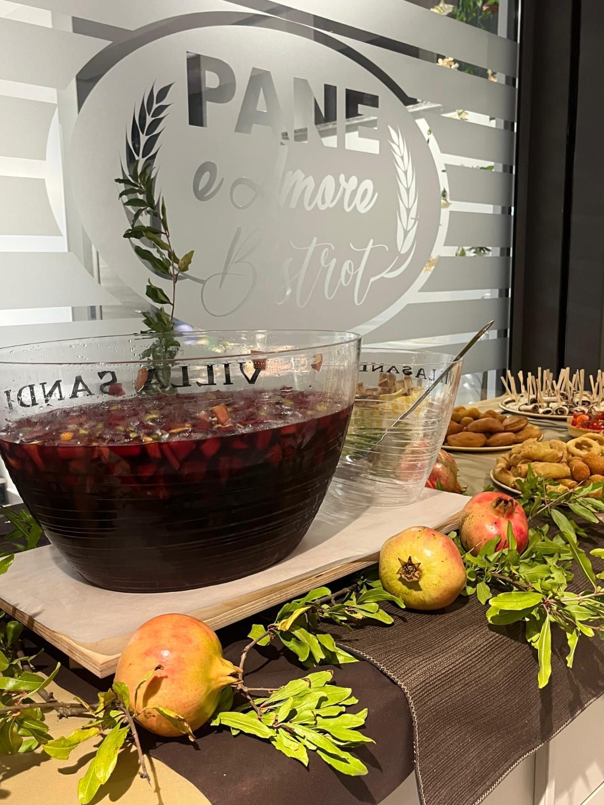 Ciotola per punch e cibo in esposizione. Ciotola con liquido rosso, melograni, rametti verdi e un'insegna smerigliata sulla finestra.