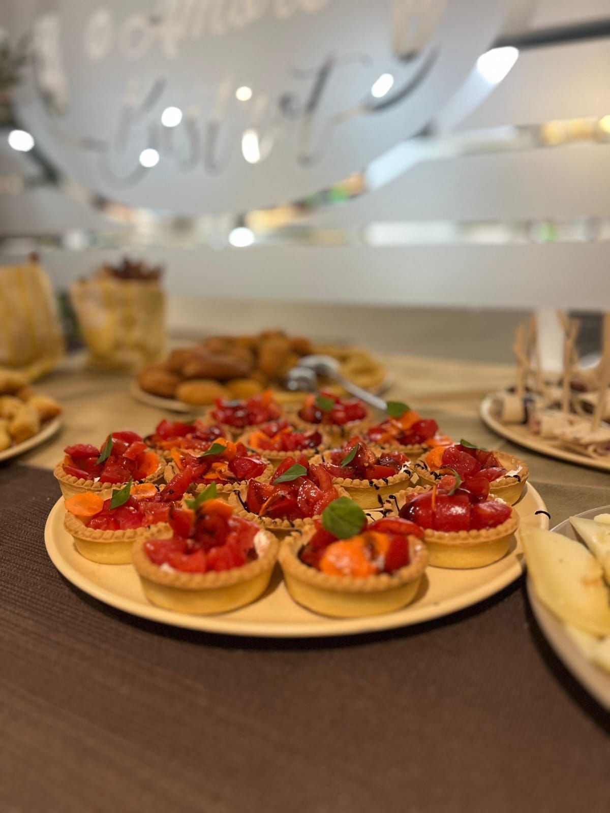 Crostate di fragole su un piatto, buffet con pasticcini, altri dessert sullo sfondo, interno.