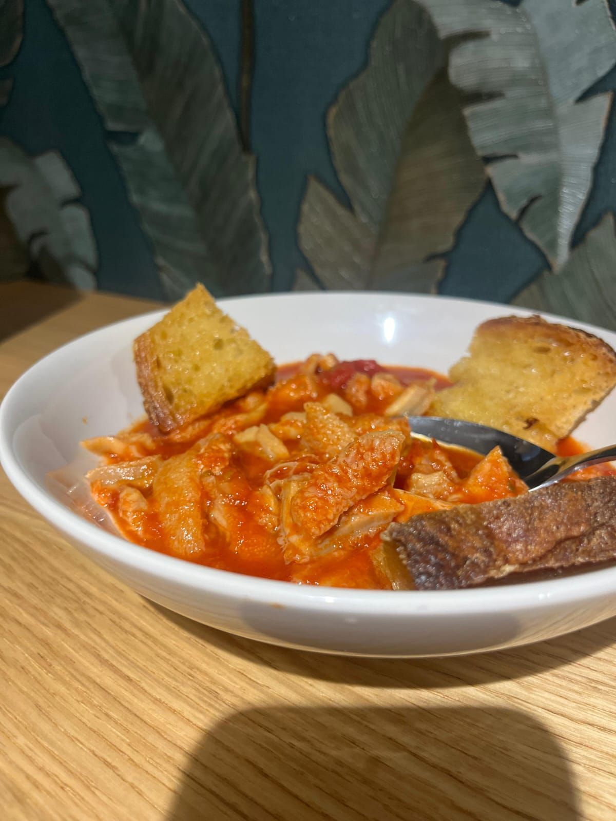 Ciotola di pasta al sugo rosso con pezzi di carne, due fette di pane tostato, su un tavolo di legno.