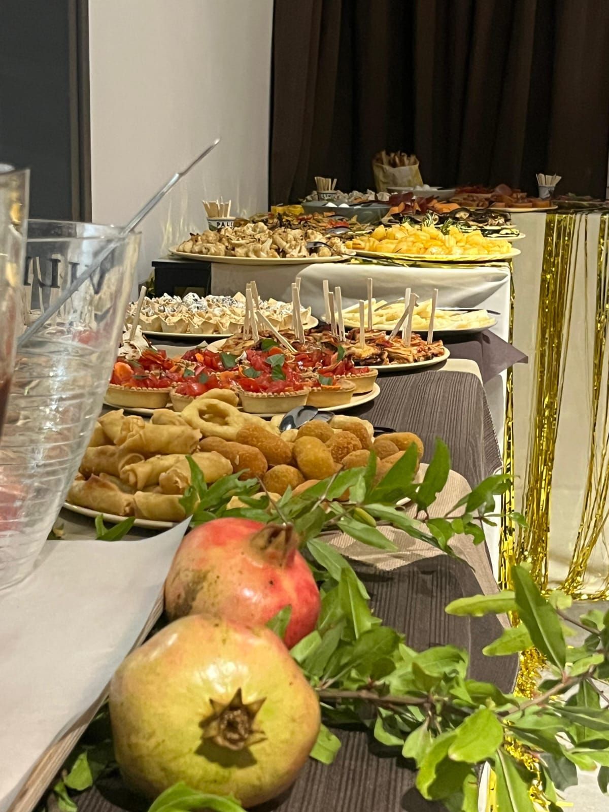Tavolo del buffet imbandito con cibo: antipasti, frutta e piante decorative.