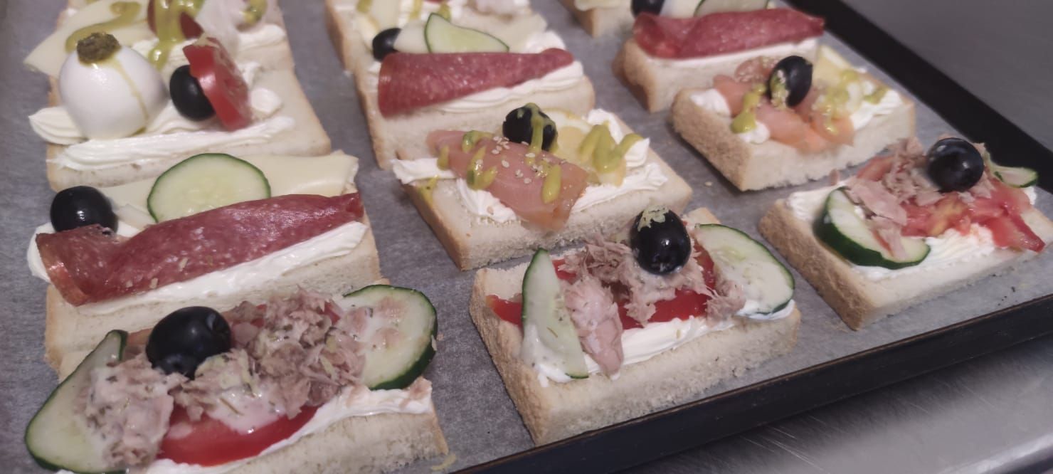 Vassoio di piccoli panini con vari condimenti: tonno, salame, cetriolo, olive e formaggio.