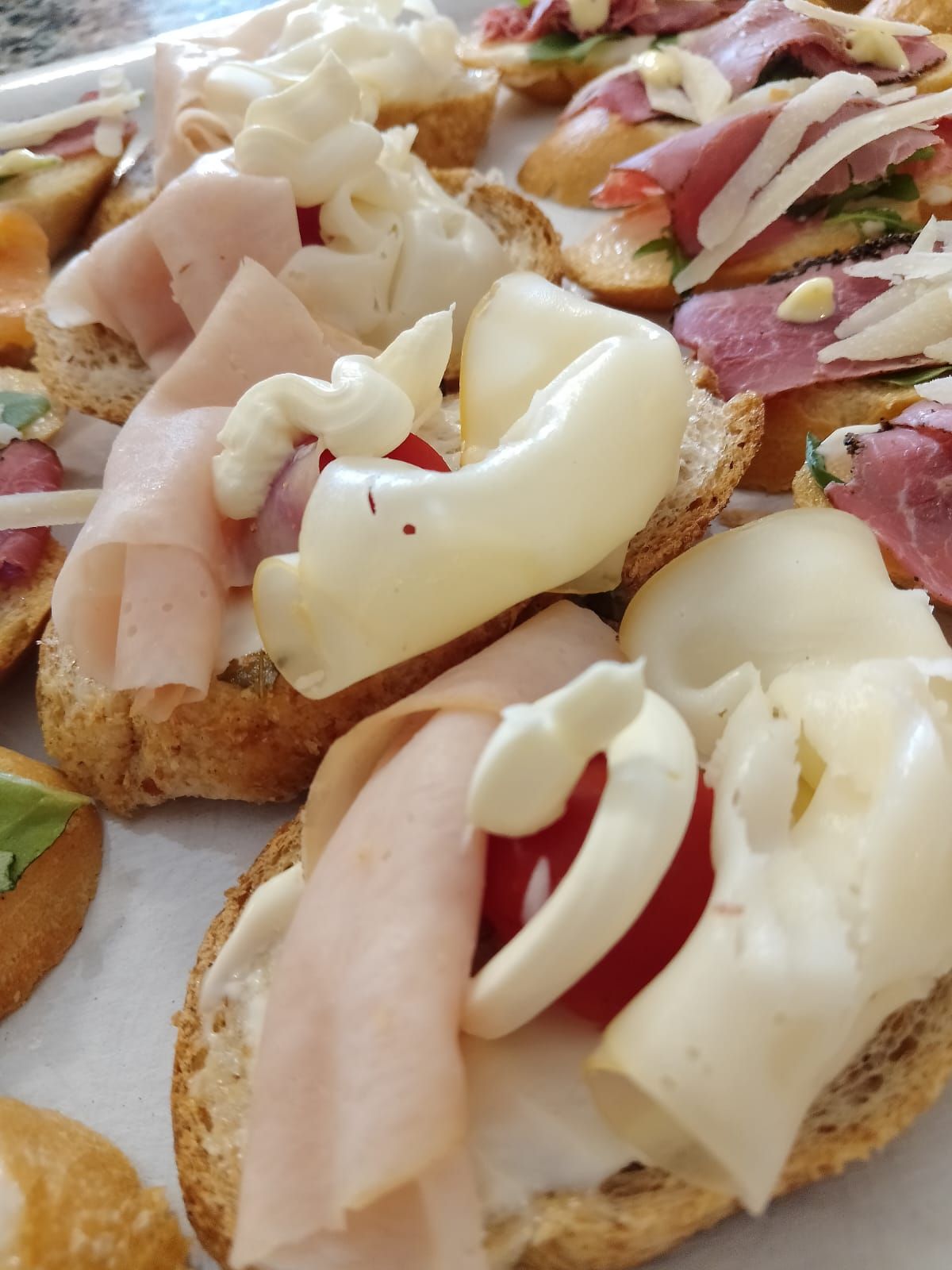 Antipasti di bruschette con condimenti come prosciutto, formaggio e pomodoro, su pane tostato.