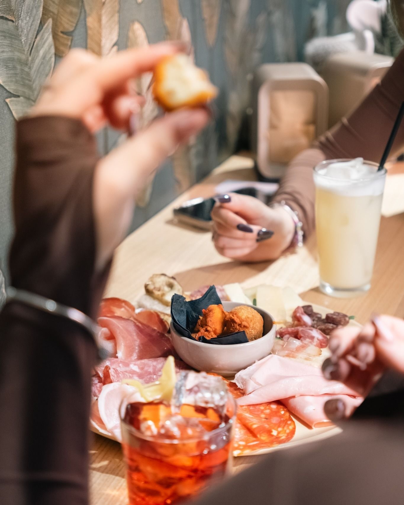 Persona che tiene in mano del pane sopra un tagliere di salumi e delle bevande su un tavolo di legno.