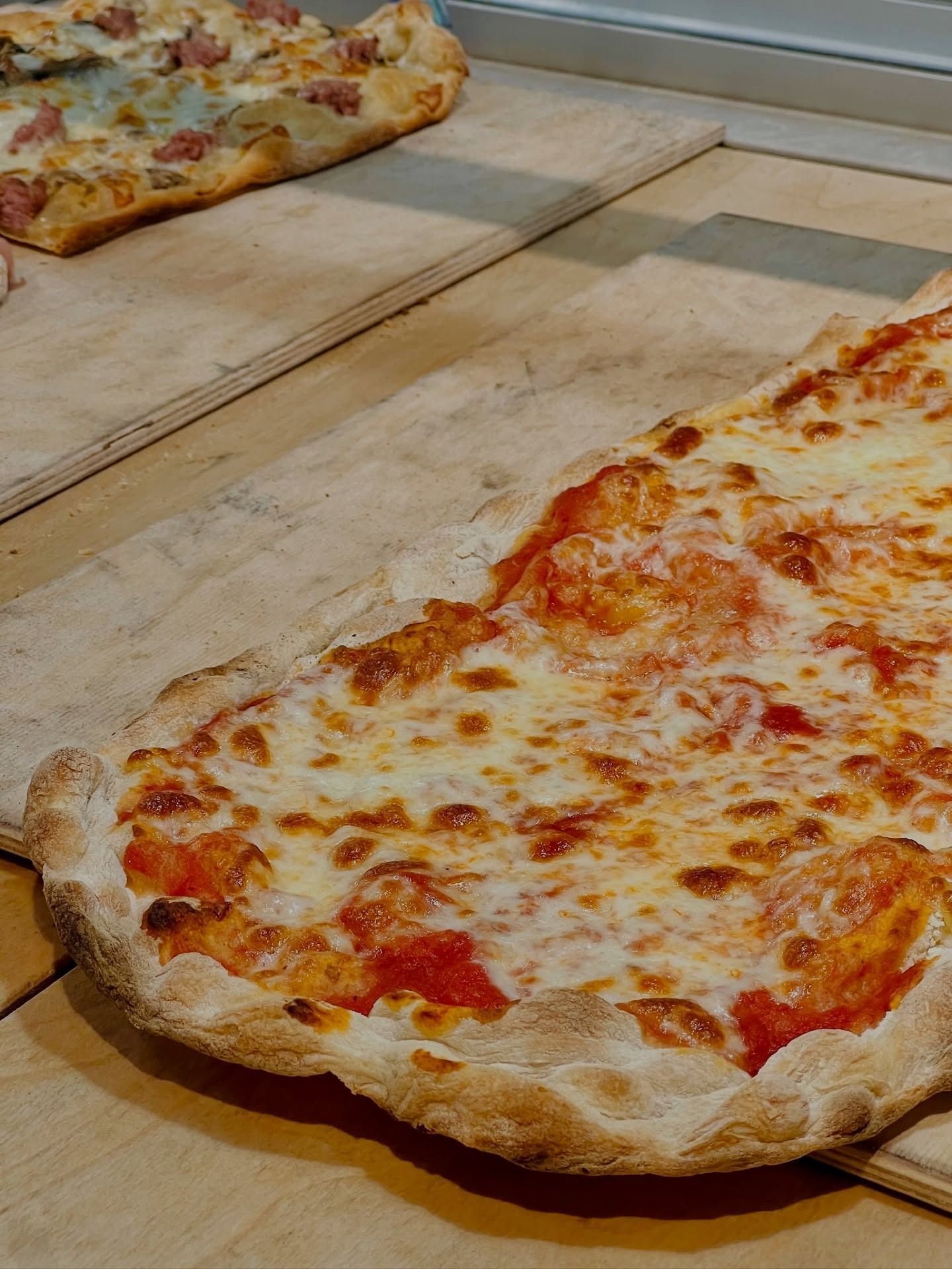 Pizza con formaggio fuso e salsa rossa, su un tagliere di legno. Un'altra pizza sullo sfondo.