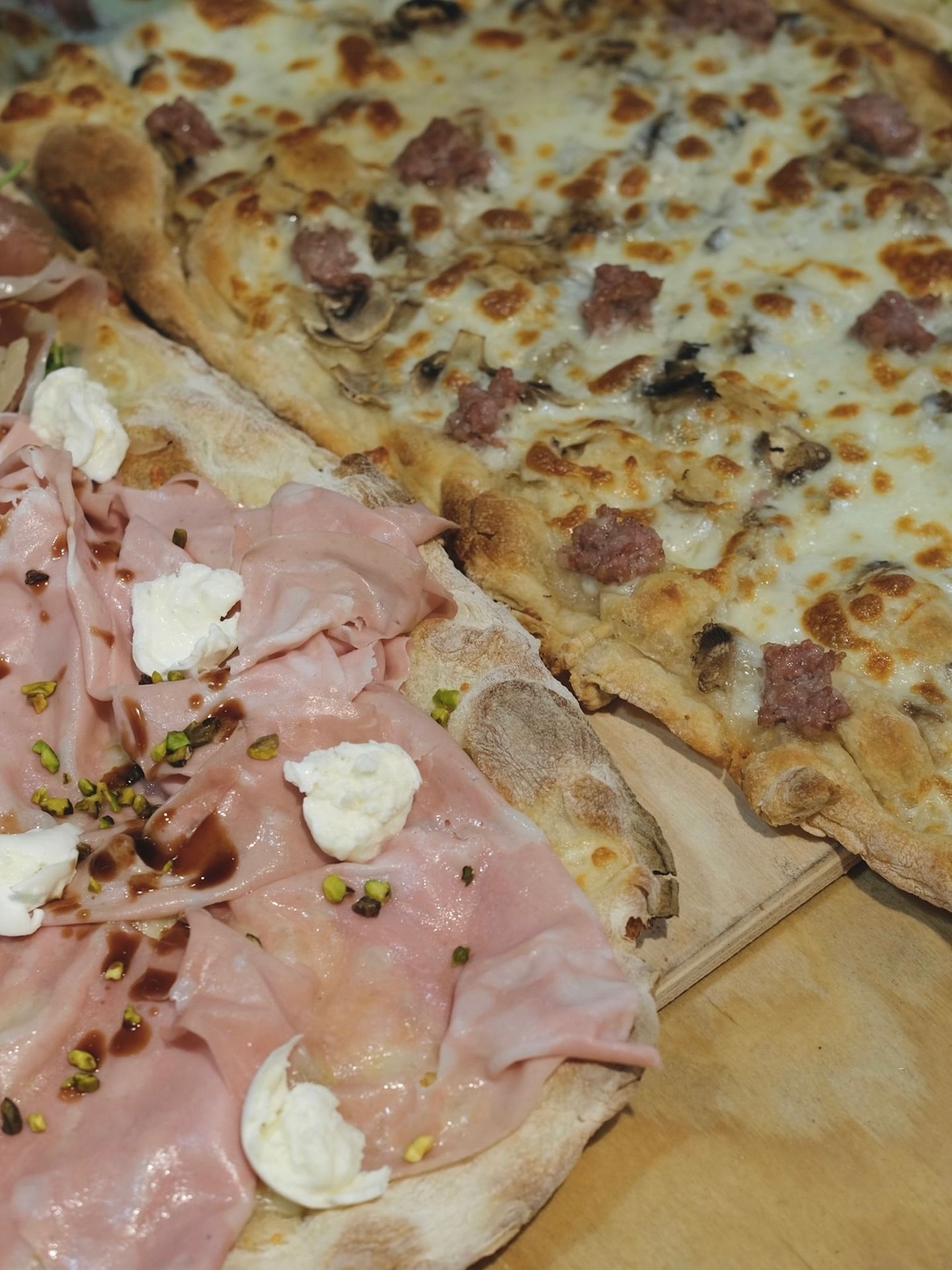 Due pizze rettangolari: una con prosciutto, formaggio e pistacchi, l'altra con salsiccia e funghi.