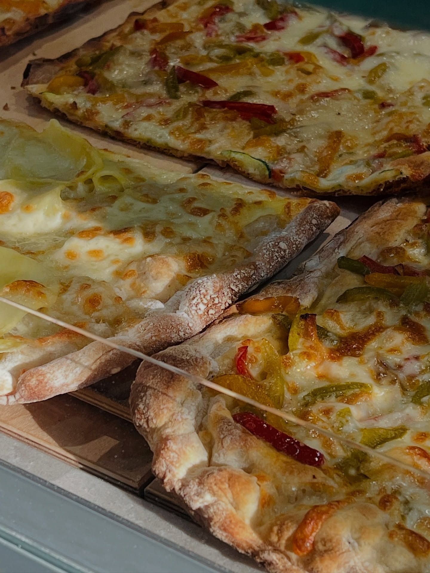 Tre fette di pizza con i condimenti, in primo piano. Si vedono le croste, con formaggio fuso e peperoni rossi/verdi.