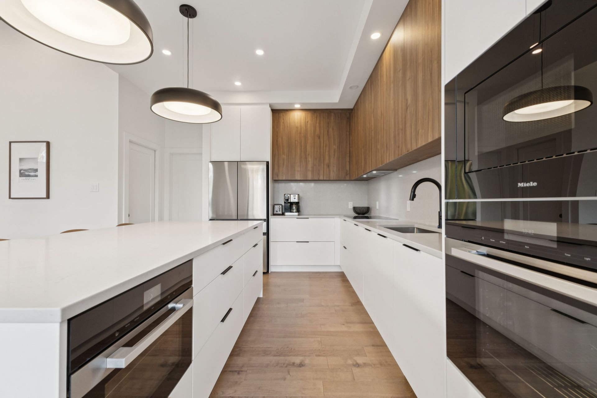 Cuisine moderne avec armoires blanches et en bois, appareils électroménagers en acier inoxydable et îlot central.