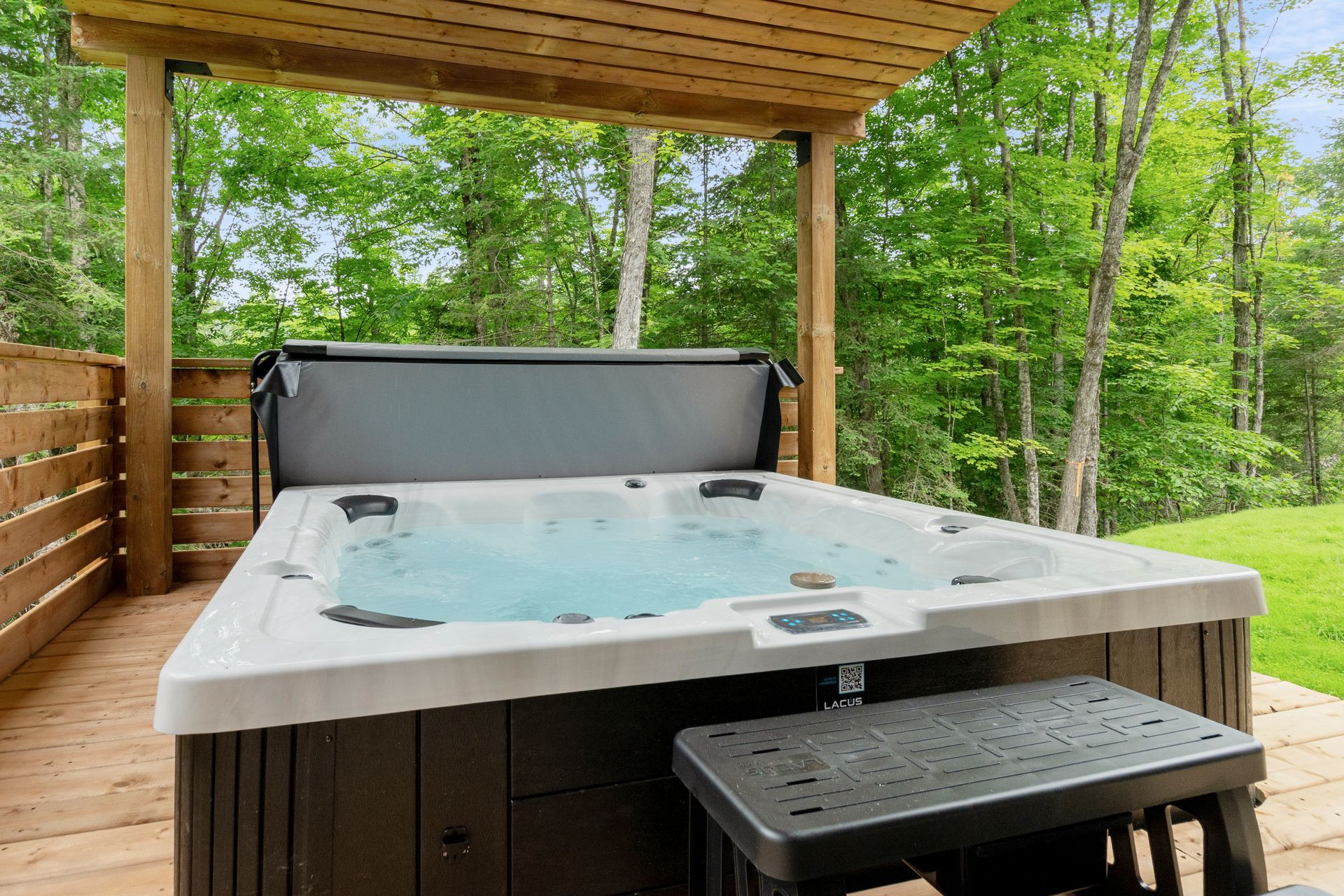 Bain à remous sur une terrasse en bois, abritée par une pergola en bois, dans un cadre boisé.