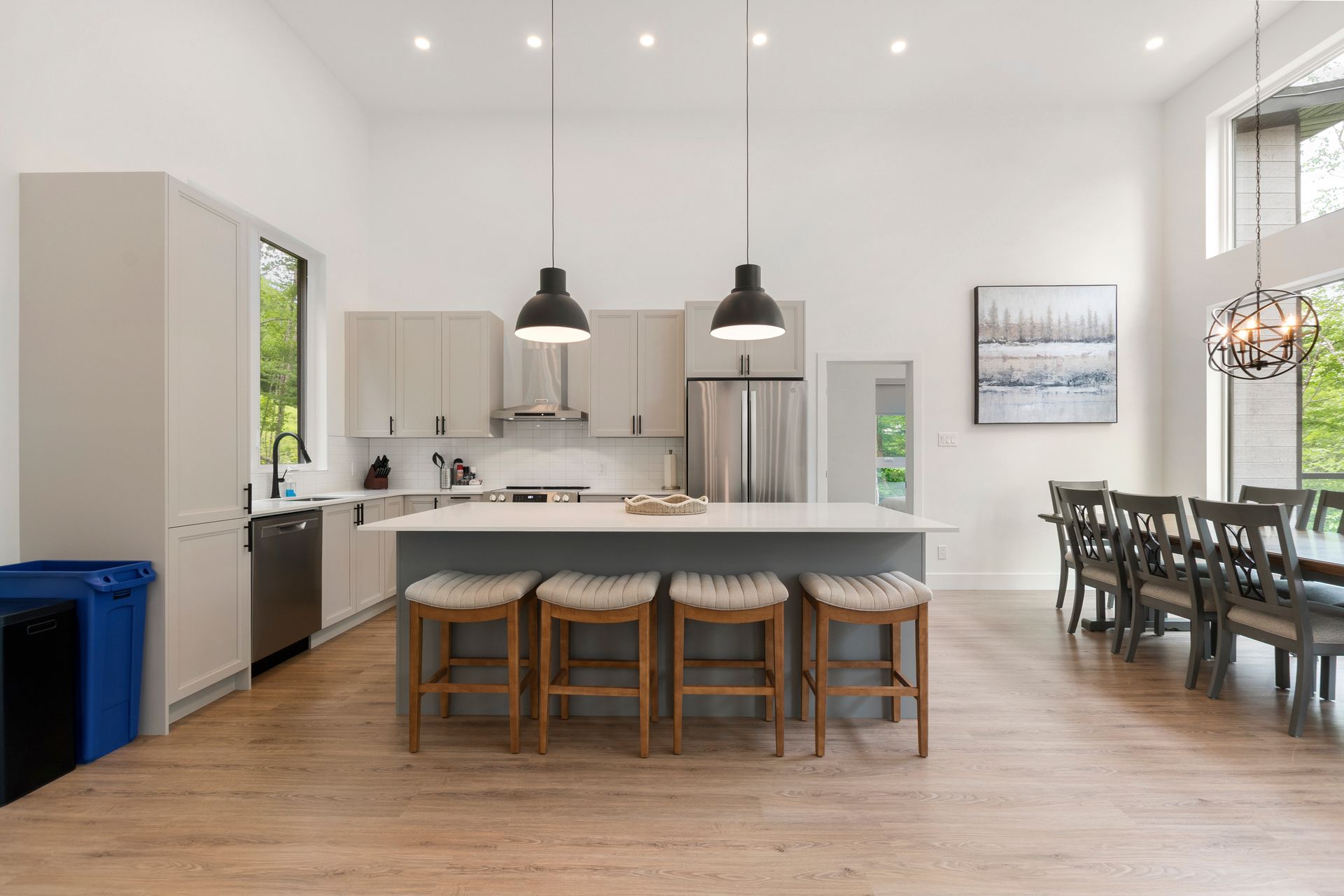 Cuisine moderne avec îlot central, coin repas et coin salon ; parquet clair, placards gris, électroménager en inox.