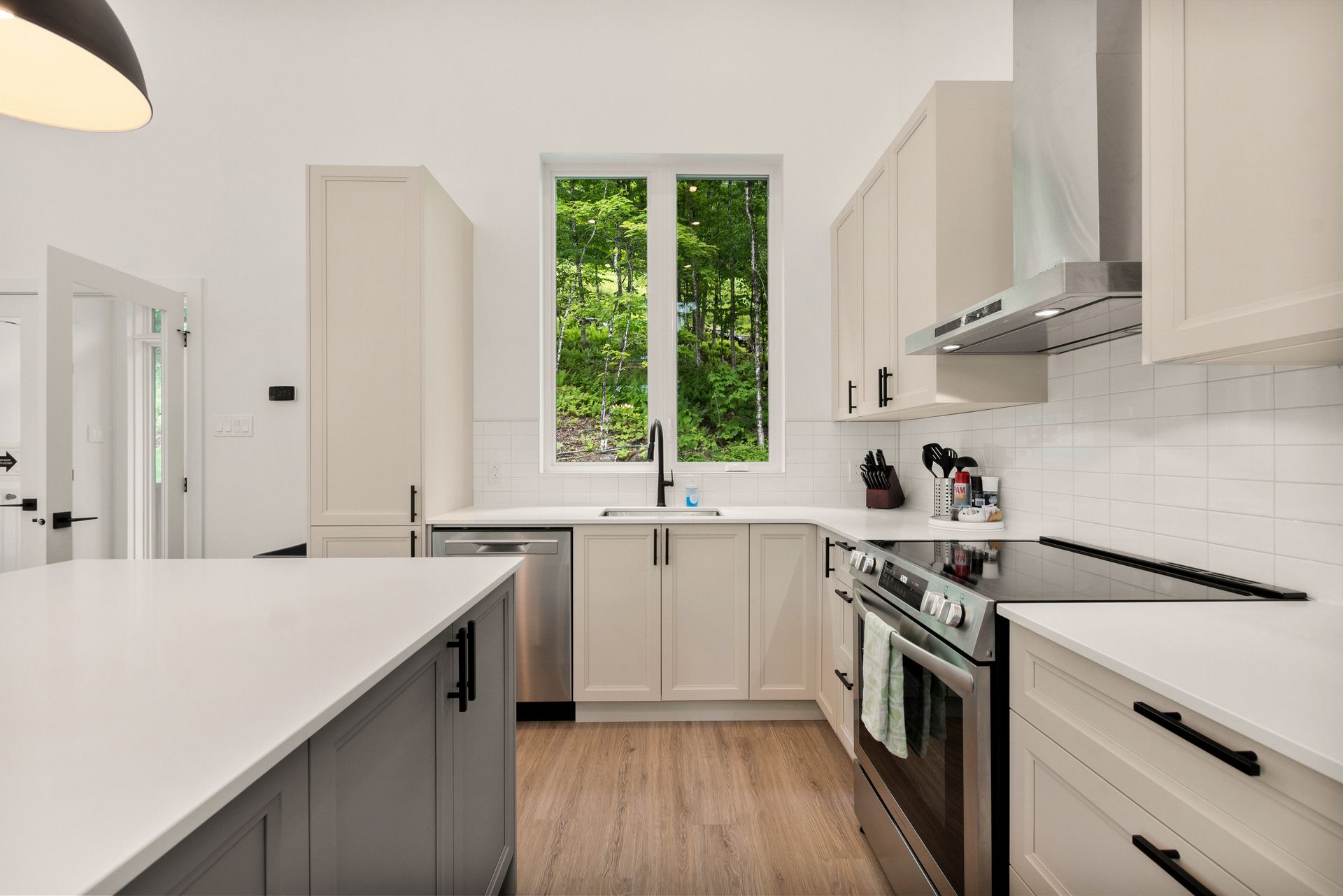 Cuisine moderne avec placards blancs, îlot gris et fenêtre donnant sur la verdure.