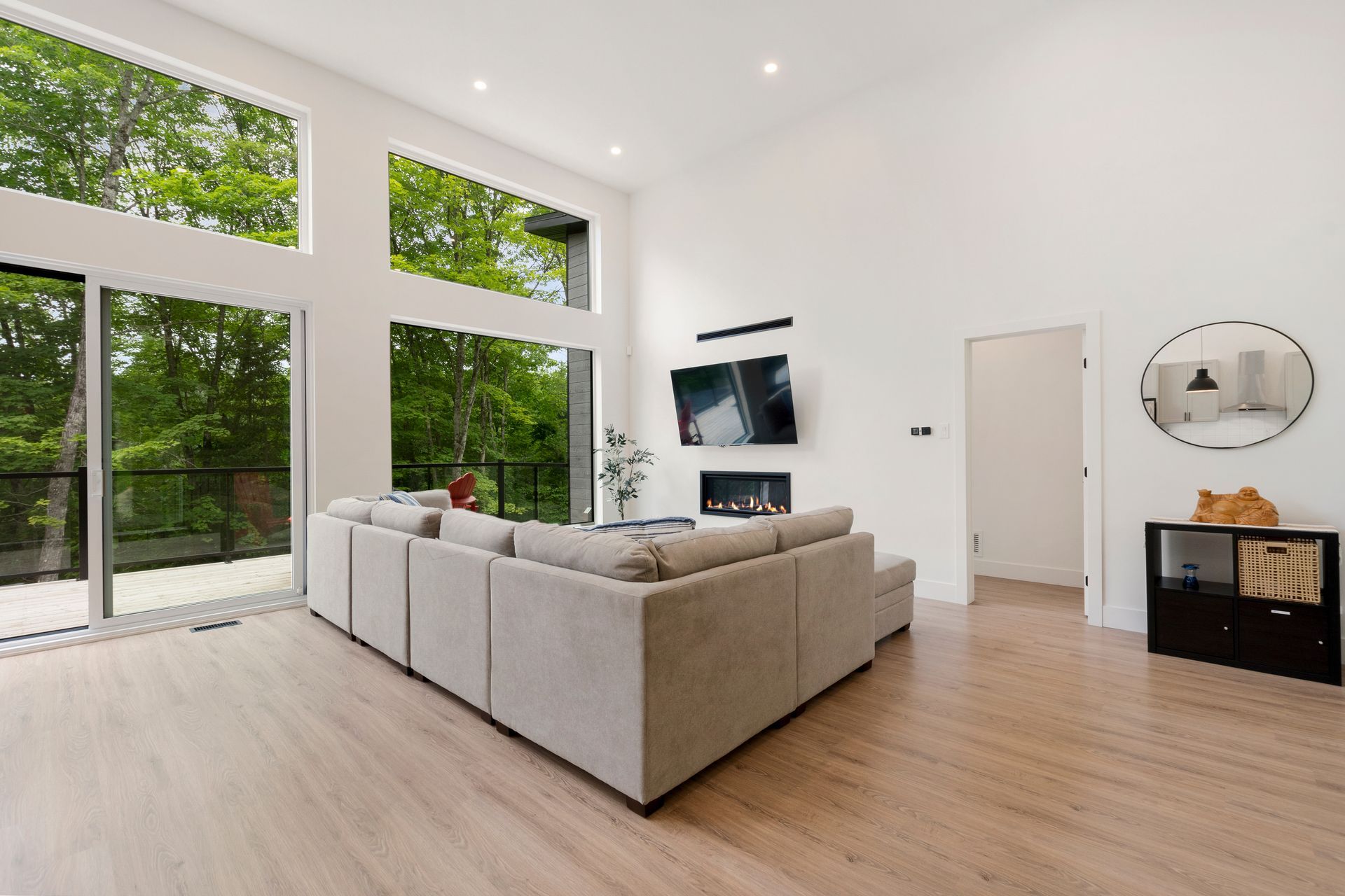 Salon spacieux avec de grandes fenêtres donnant sur les arbres, un canapé d'angle moderne et une cheminée.