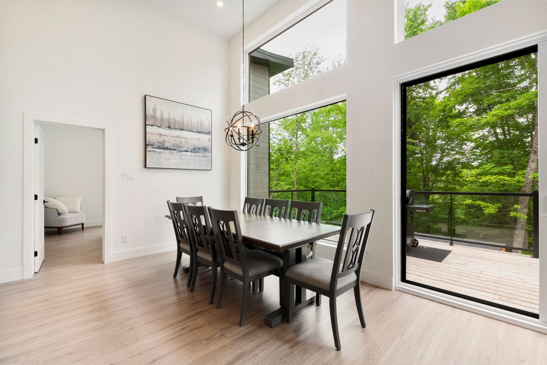 Salle à manger avec de grandes fenêtres donnant sur les arbres ; table avec chaises, œuvres d'art et lustre.