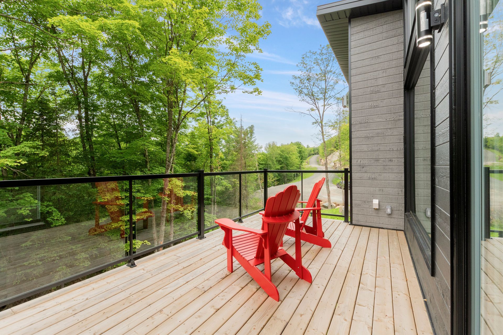 Deux chaises Adirondack rouges sur une terrasse en bois donnant sur une végétation luxuriante et une étendue d'eau calme.