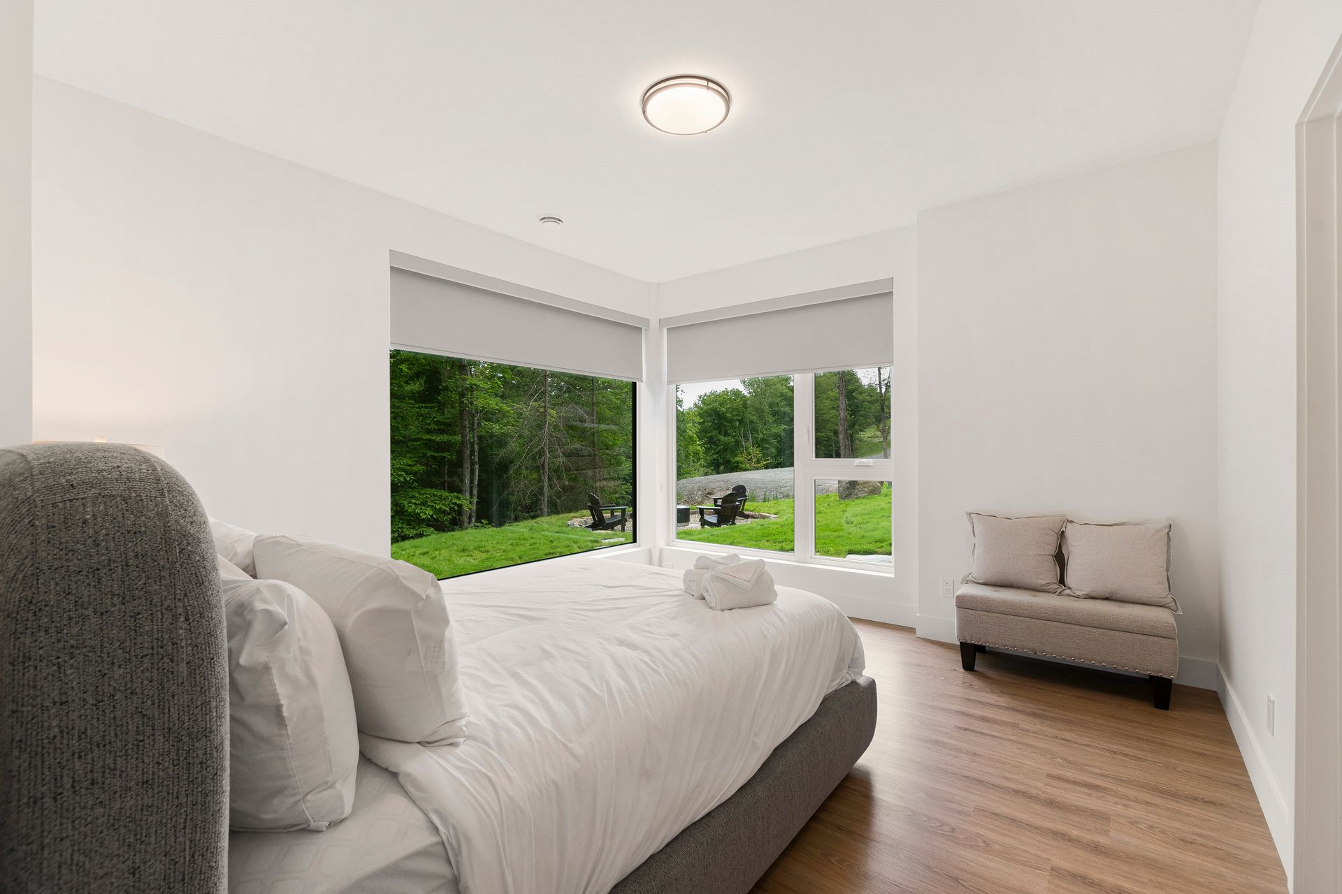 Chambre avec de grandes fenêtres, un lit et un banc, donnant sur une pelouse verdoyante.