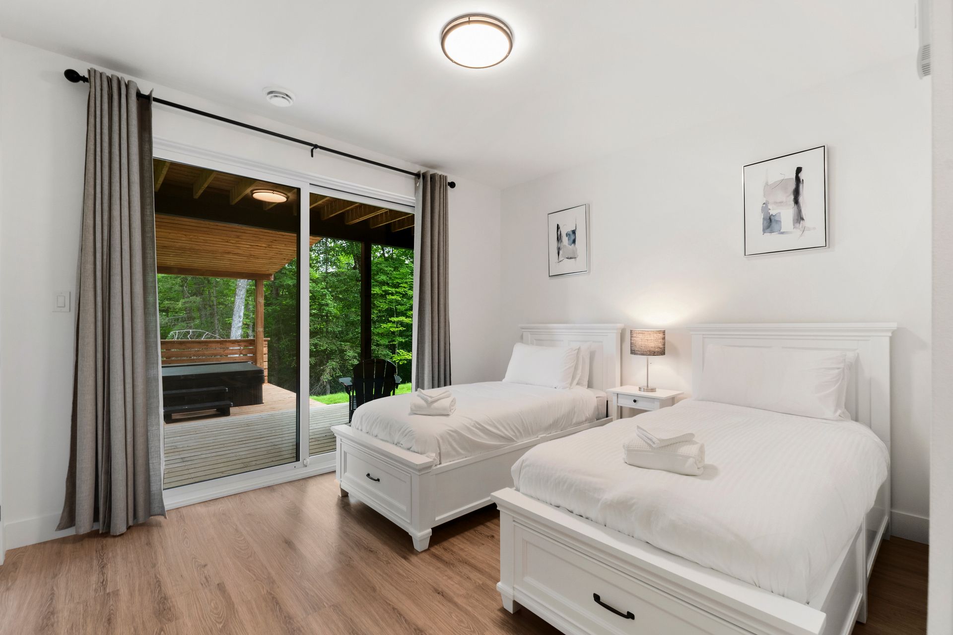 Chambre avec deux lits blancs, porte coulissante donnant sur une terrasse, parquet et rideaux gris.
