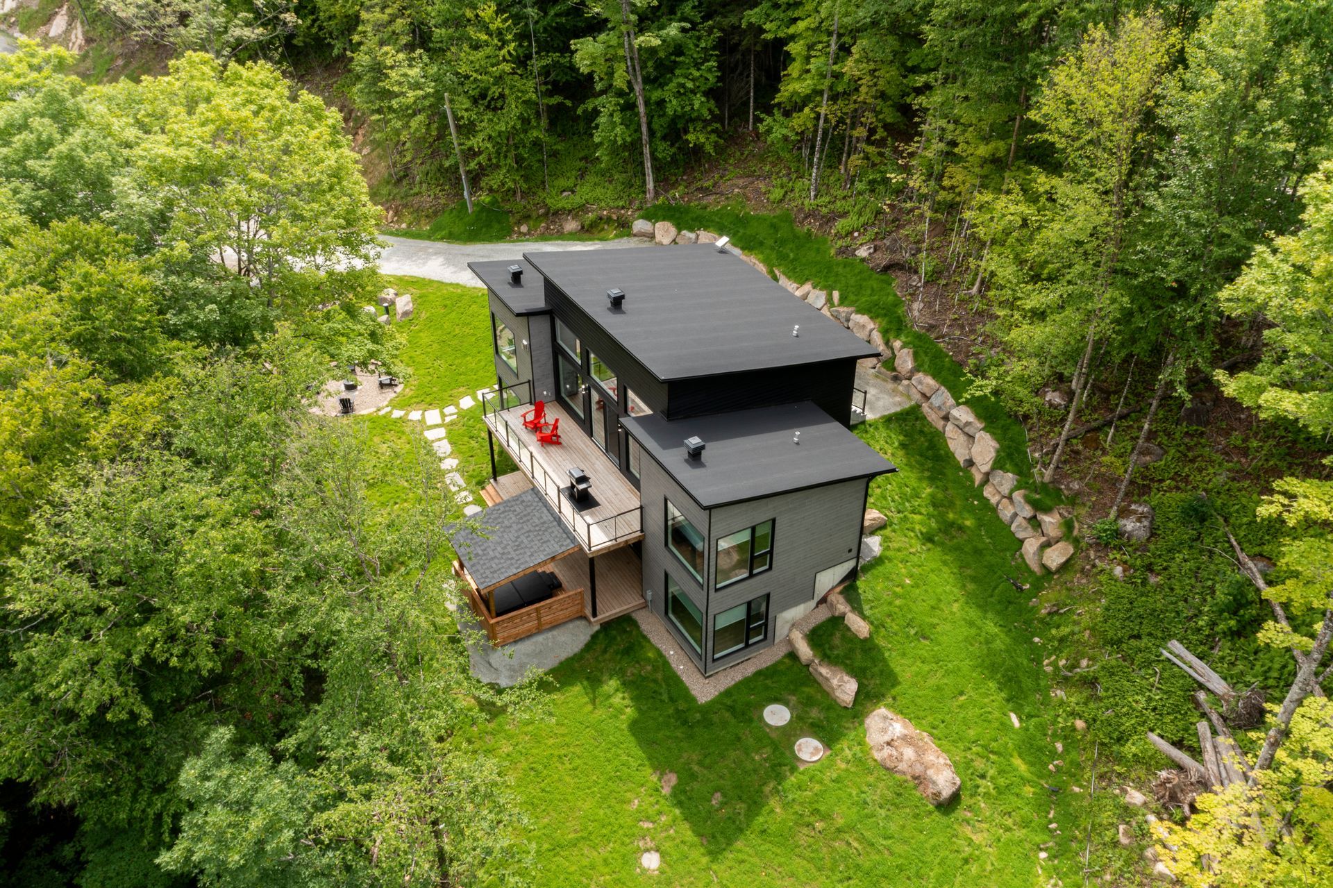 Maison grise moderne à flanc de colline, entourée d'arbres verdoyants.