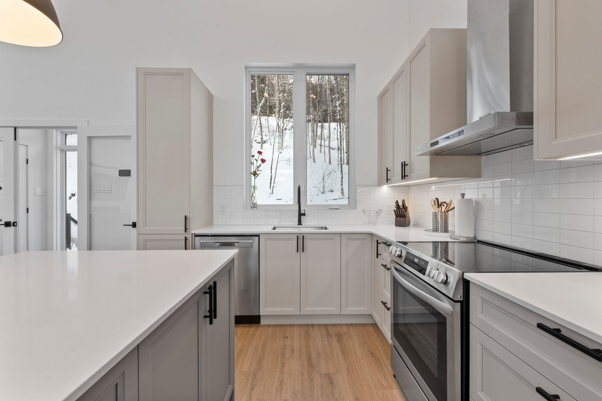 Cuisine moderne avec placards gris clair, appareils électroménagers en acier inoxydable et une fenêtre donnant sur un paysage enneigé.