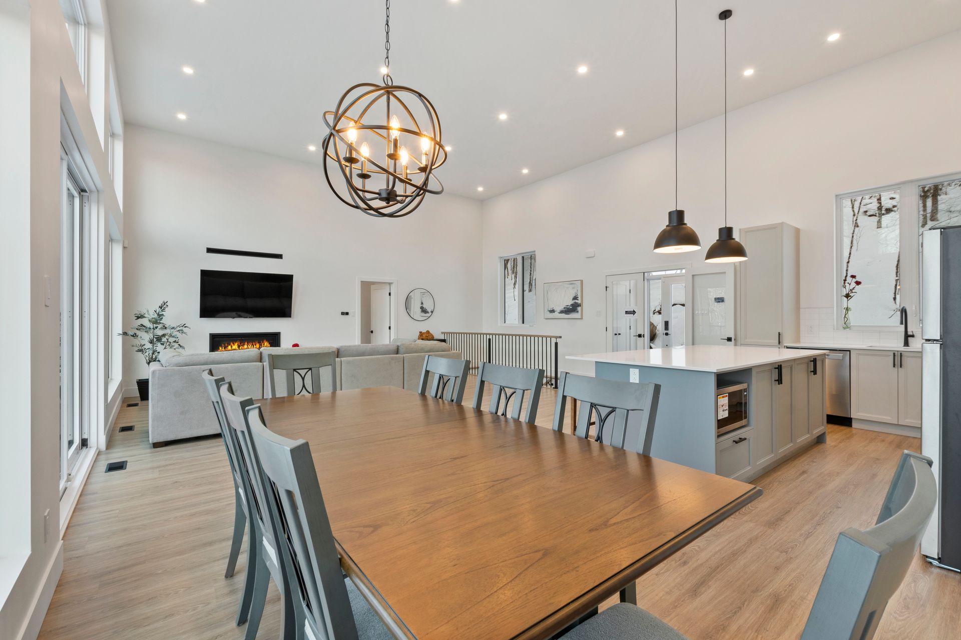 Cuisine et salle à manger spacieuses à aire ouverte avec une longue table en bois, un îlot et de grandes fenêtres.