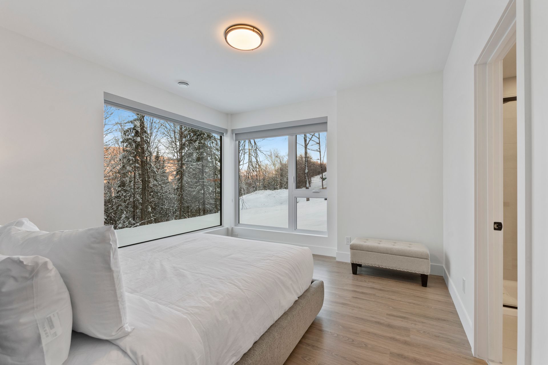 Chambre avec de grandes fenêtres, un lit, un banc et une vue sur un paysage enneigé.