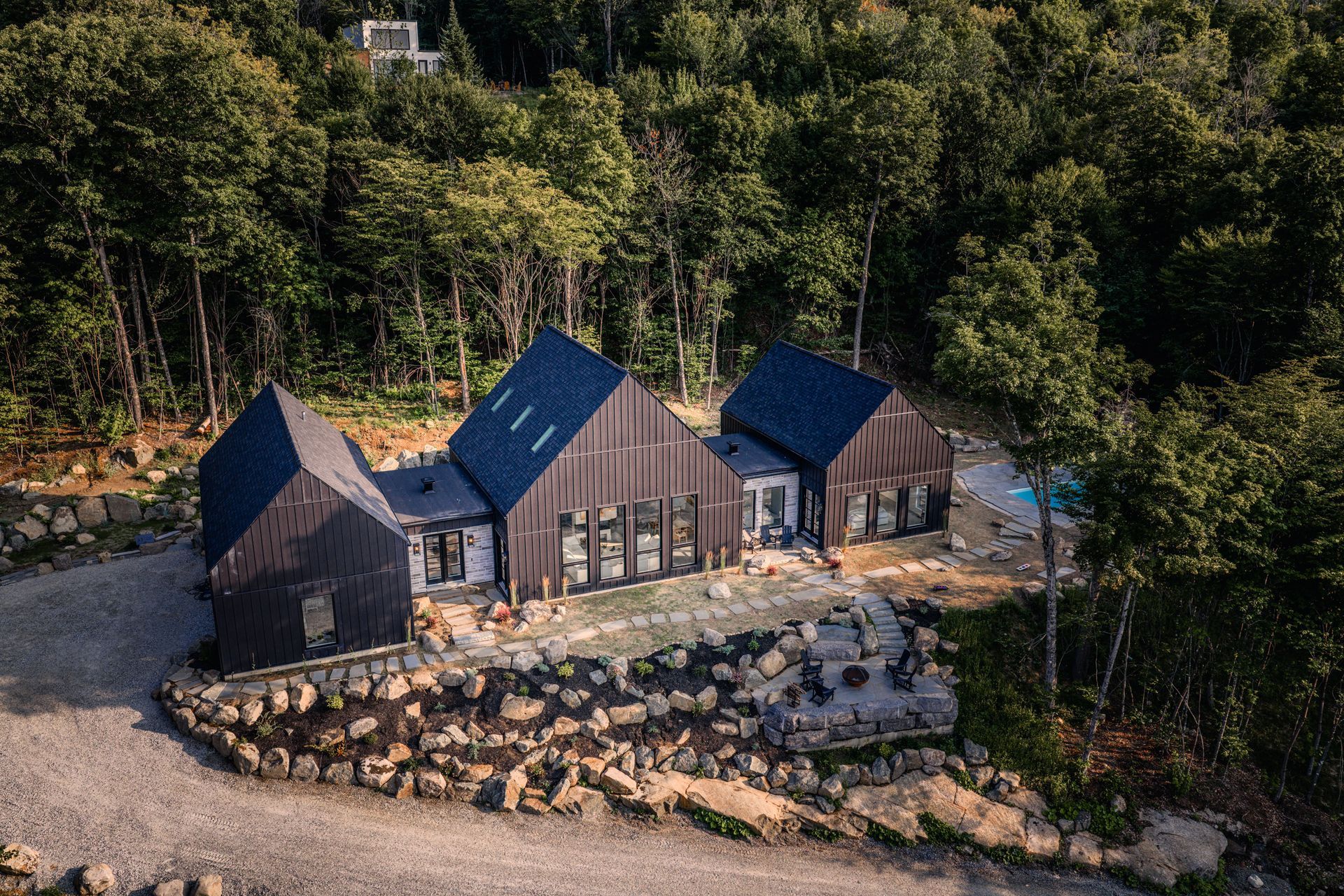Chalet moderne noir en pleine forêt ; terrasse et allée en pierre grise à l'avant.