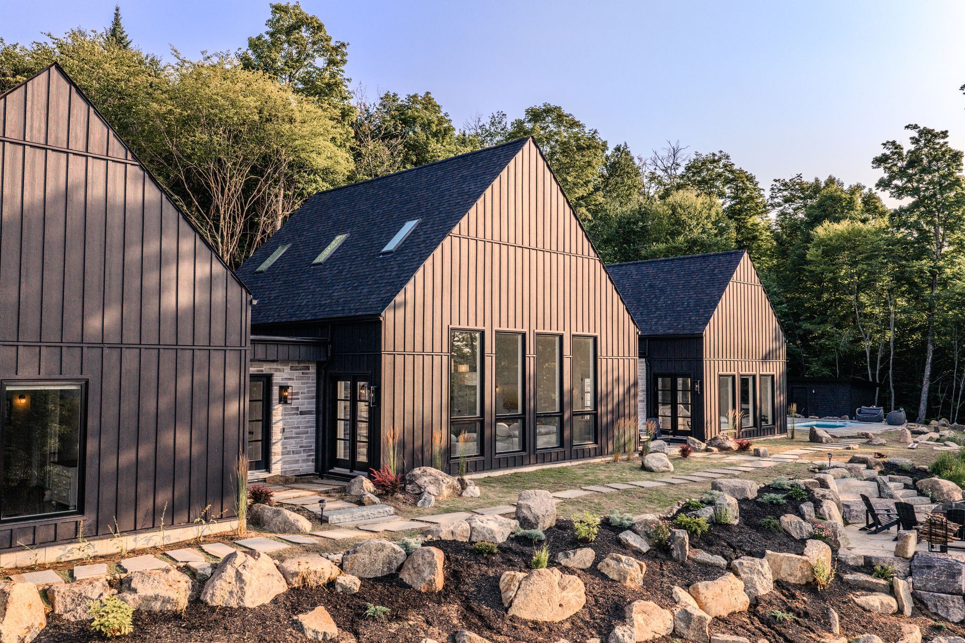 Maisons modernes noires aux toits en pente, entourées d'arbres et de rochers.