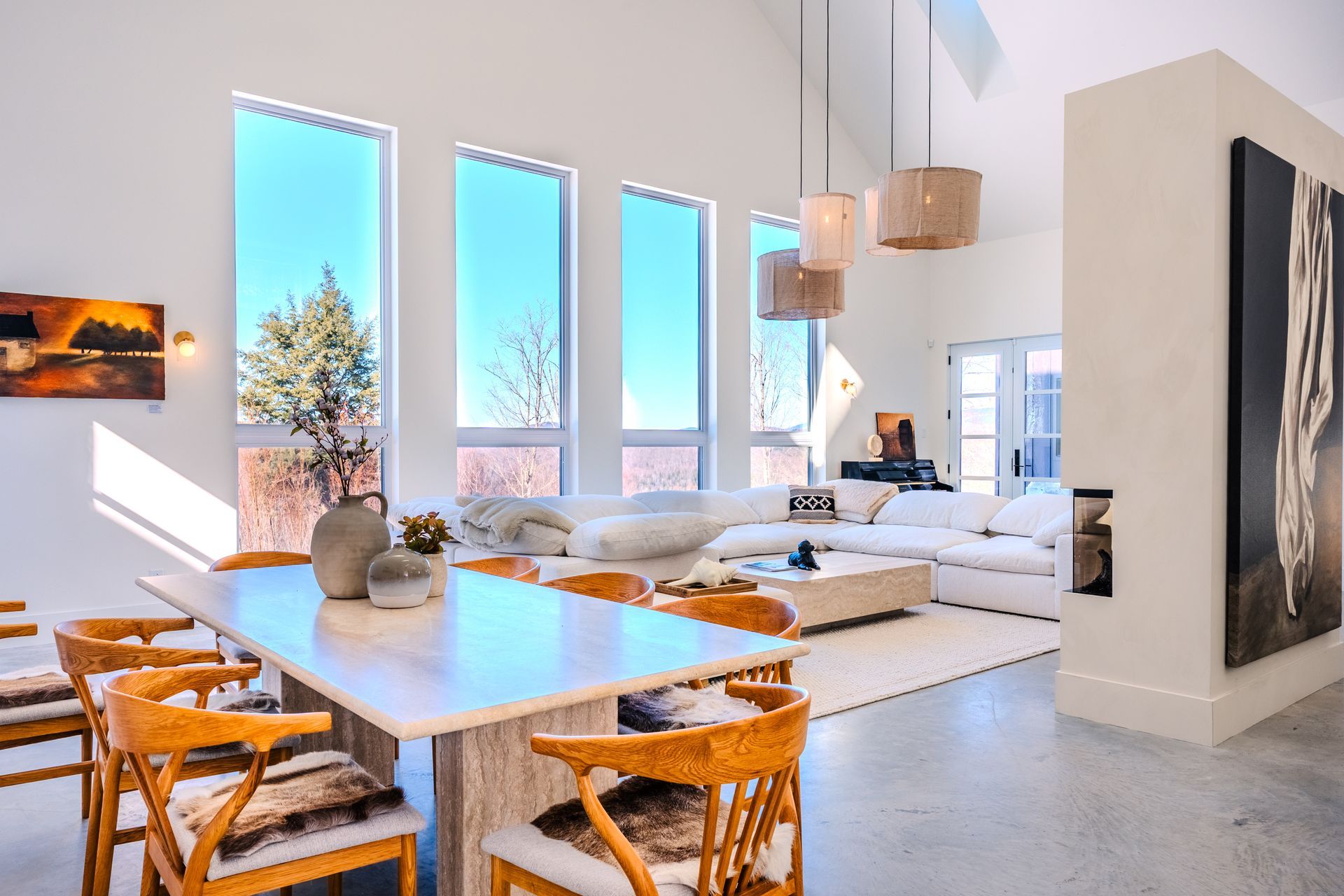 Salle à manger et salon lumineux et modernes avec de grandes fenêtres, des meubles clairs et une longue table.