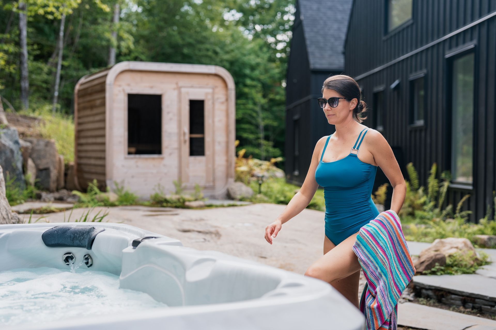 Femme en maillot de bain bleu avec une serviette, près d'un jacuzzi et d'une structure en bois.