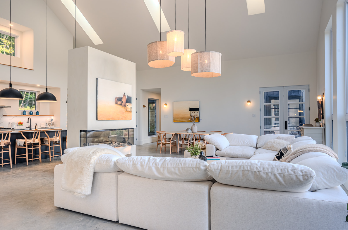 Salon spacieux et moderne avec canapé d'angle blanc, cheminée et cuisine ouverte.