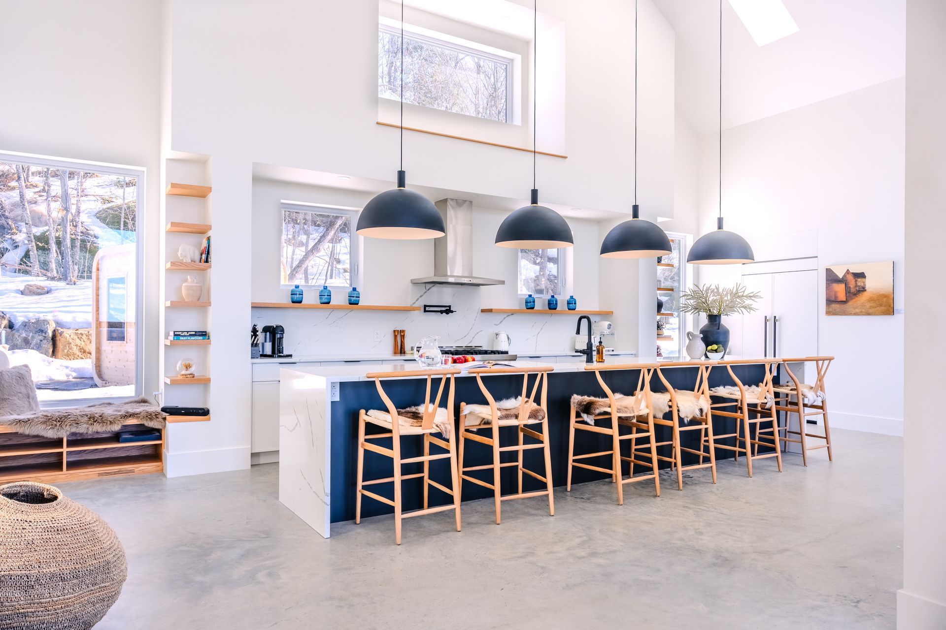 Cuisine moderne avec grand îlot central, suspensions lumineuses et fenêtre donnant sur un paysage enneigé.