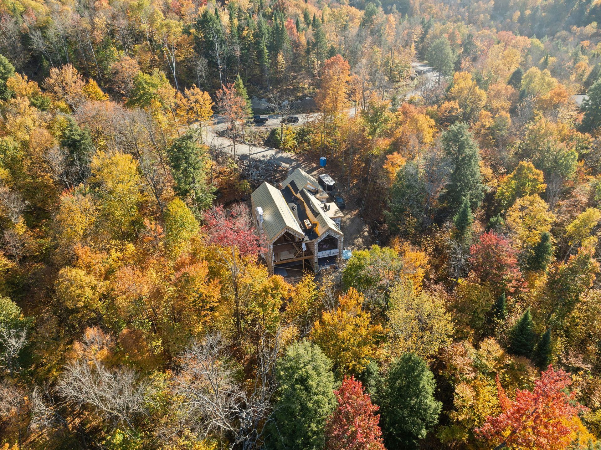 Vue aérienne d'une maison en construction, entourée d'un feuillage d'automne aux couleurs chatoyantes.