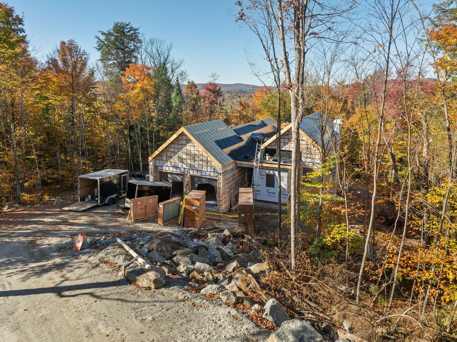 Construction d'une maison au toit partiellement construit, entourée de feuillage d'automne.