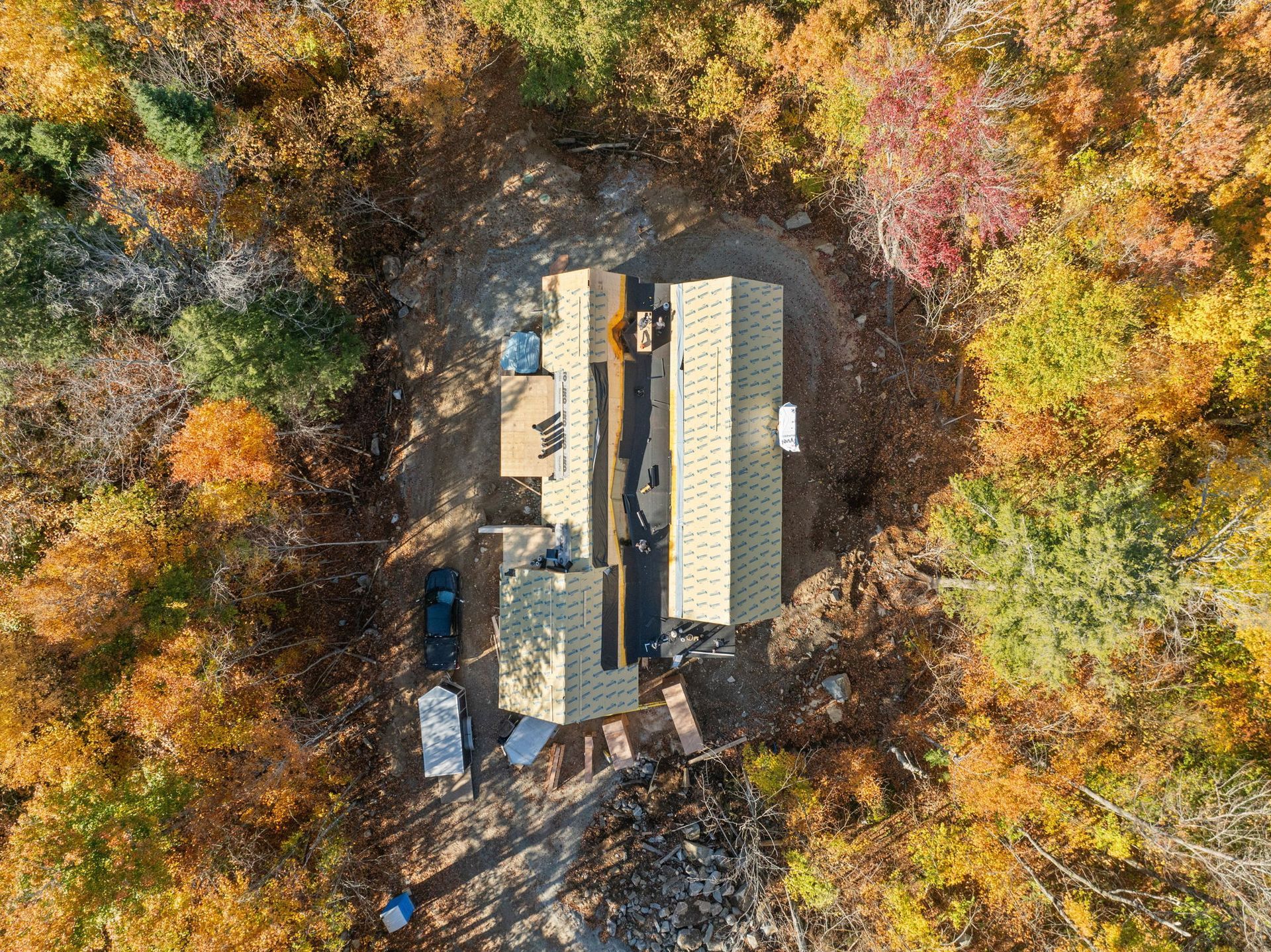 Vue aérienne d'une maison en construction entourée d'arbres aux couleurs automnales.