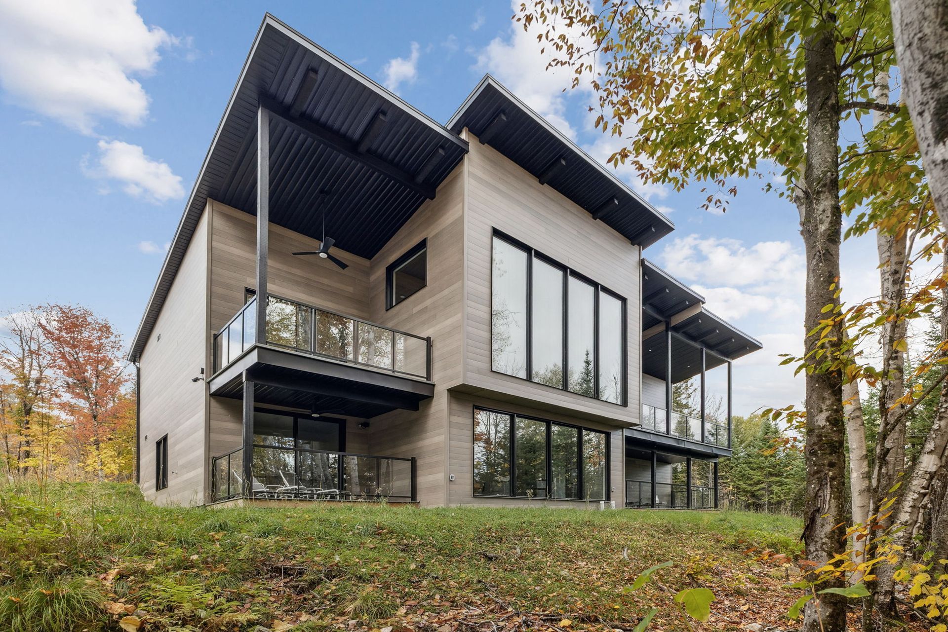 Maison moderne à deux étages avec toit sombre et grandes fenêtres donnant sur une forêt.