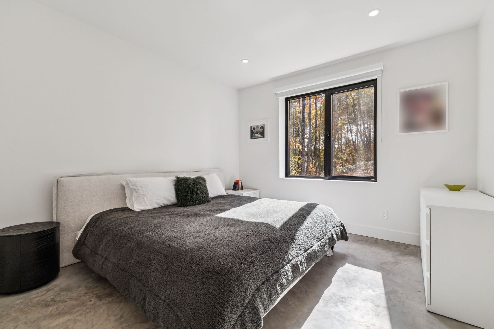 Chambre avec lit, table de chevet, fenêtre et murs blancs.